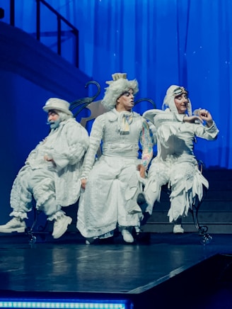 Three performers in white costumes on stage.