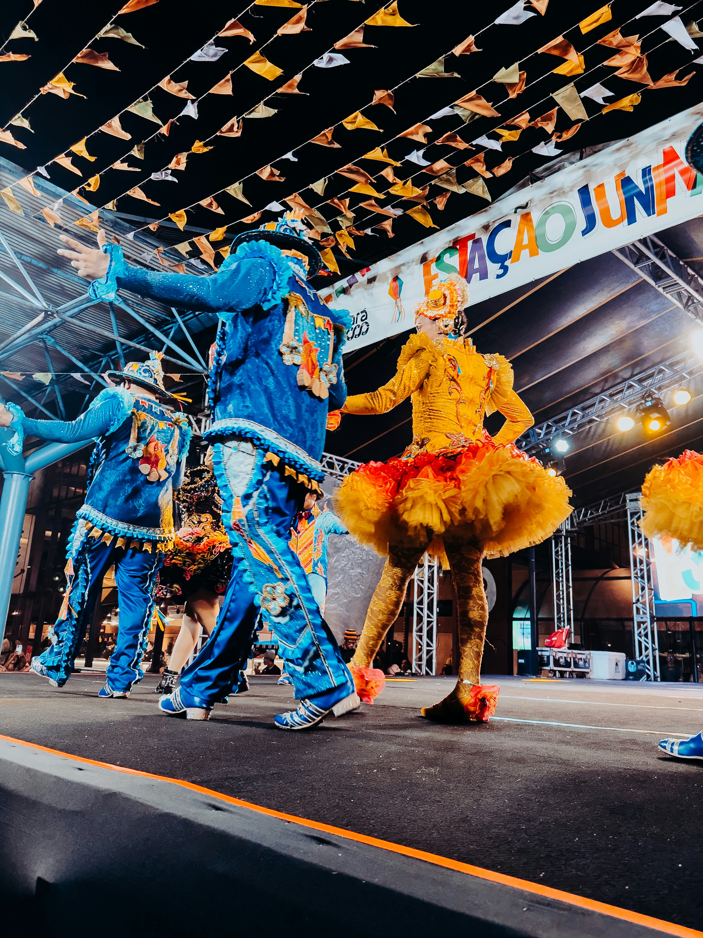Performers in colorful traditional costumes dance on an outdoor stage at night.