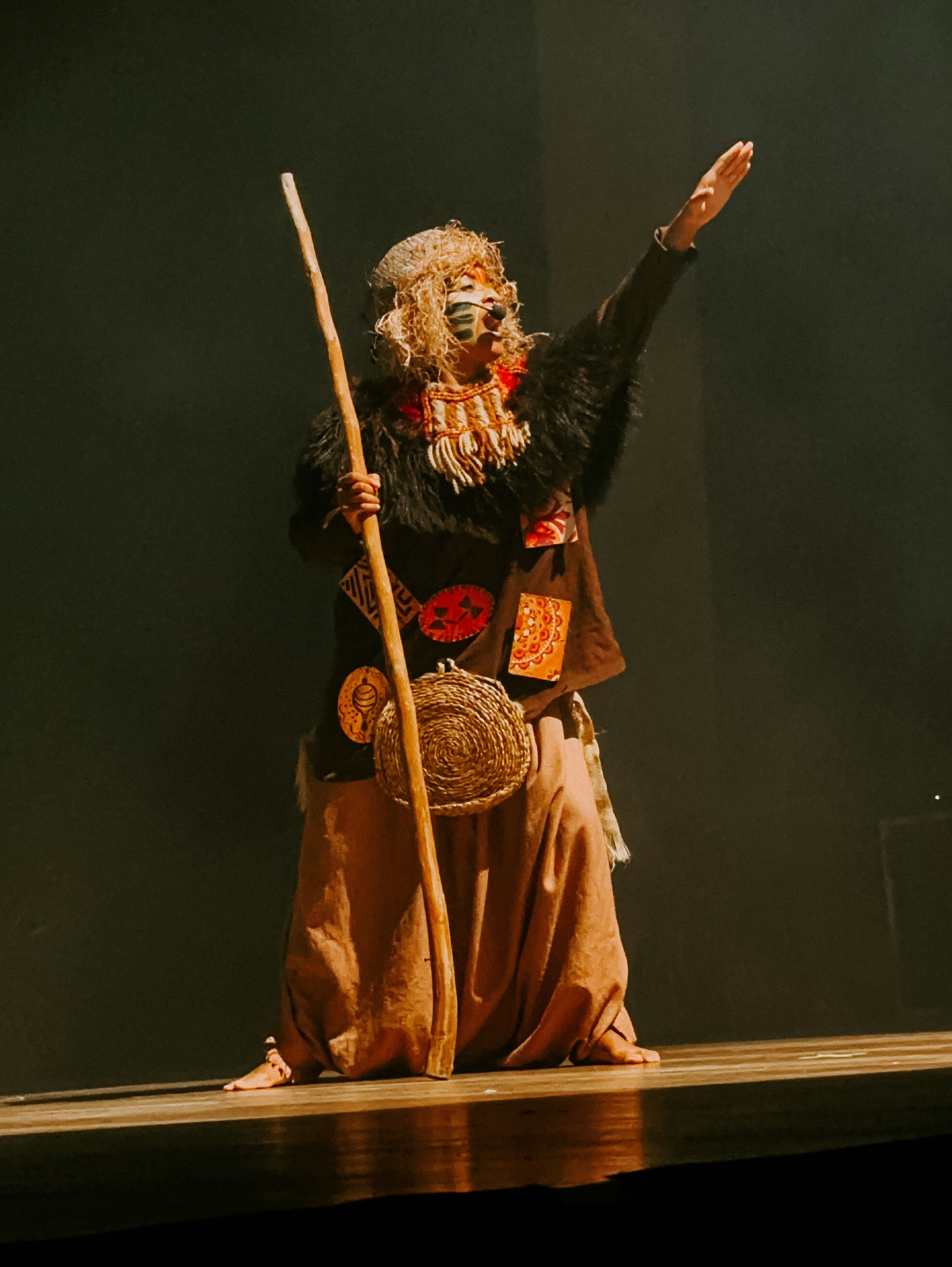 El intérprete, con máscara y disfraz tradicionales, sostiene un bastón.