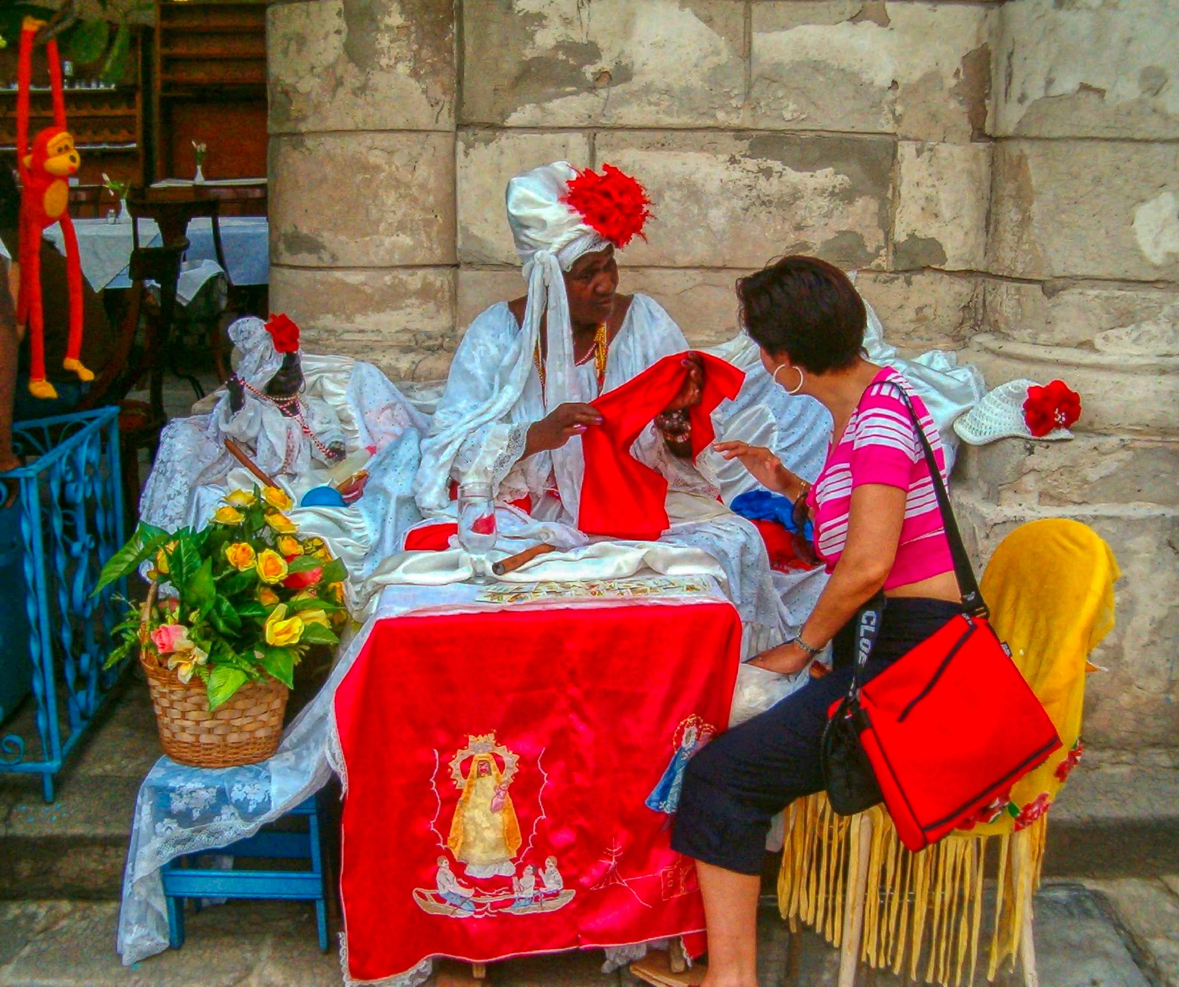 Two performers in white robes and red headwraps sit at a red-draped table with a visitor nearby.