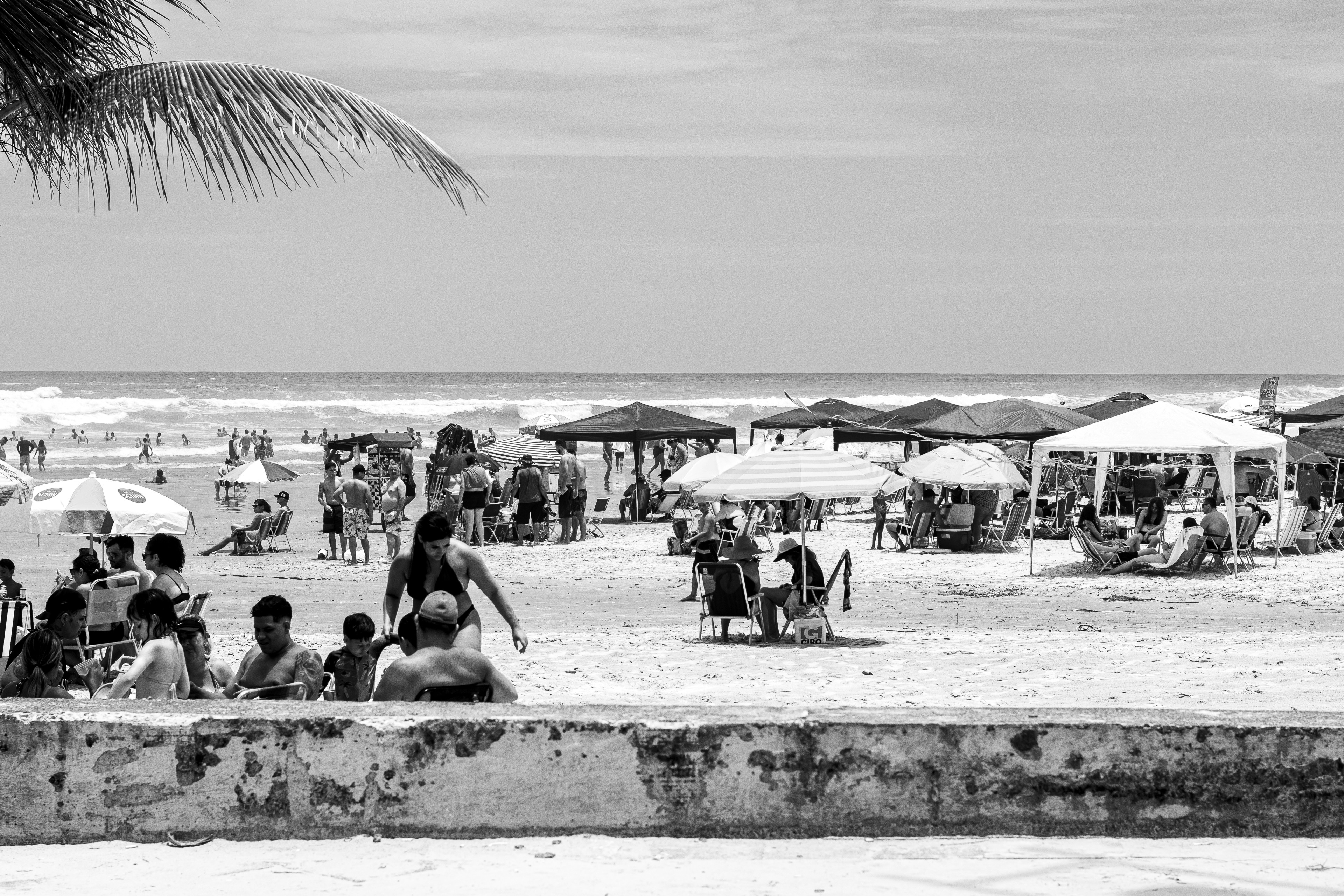 A group of people are enjoying a sunny day at the beach, with some swimming in the ocean and others relaxing under umbrellas on the sand.