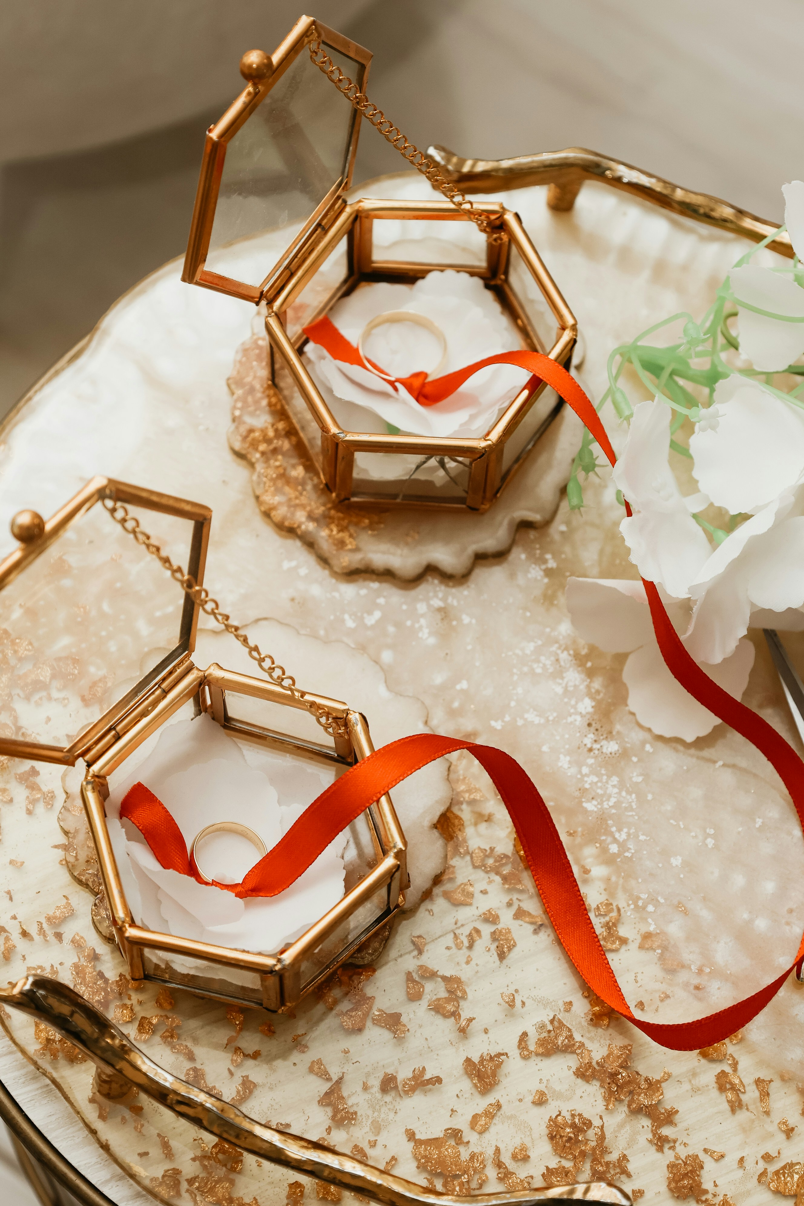 Duas caixas hexagonais de vidro abrigam alianças de casamento com fitas vermelhas.