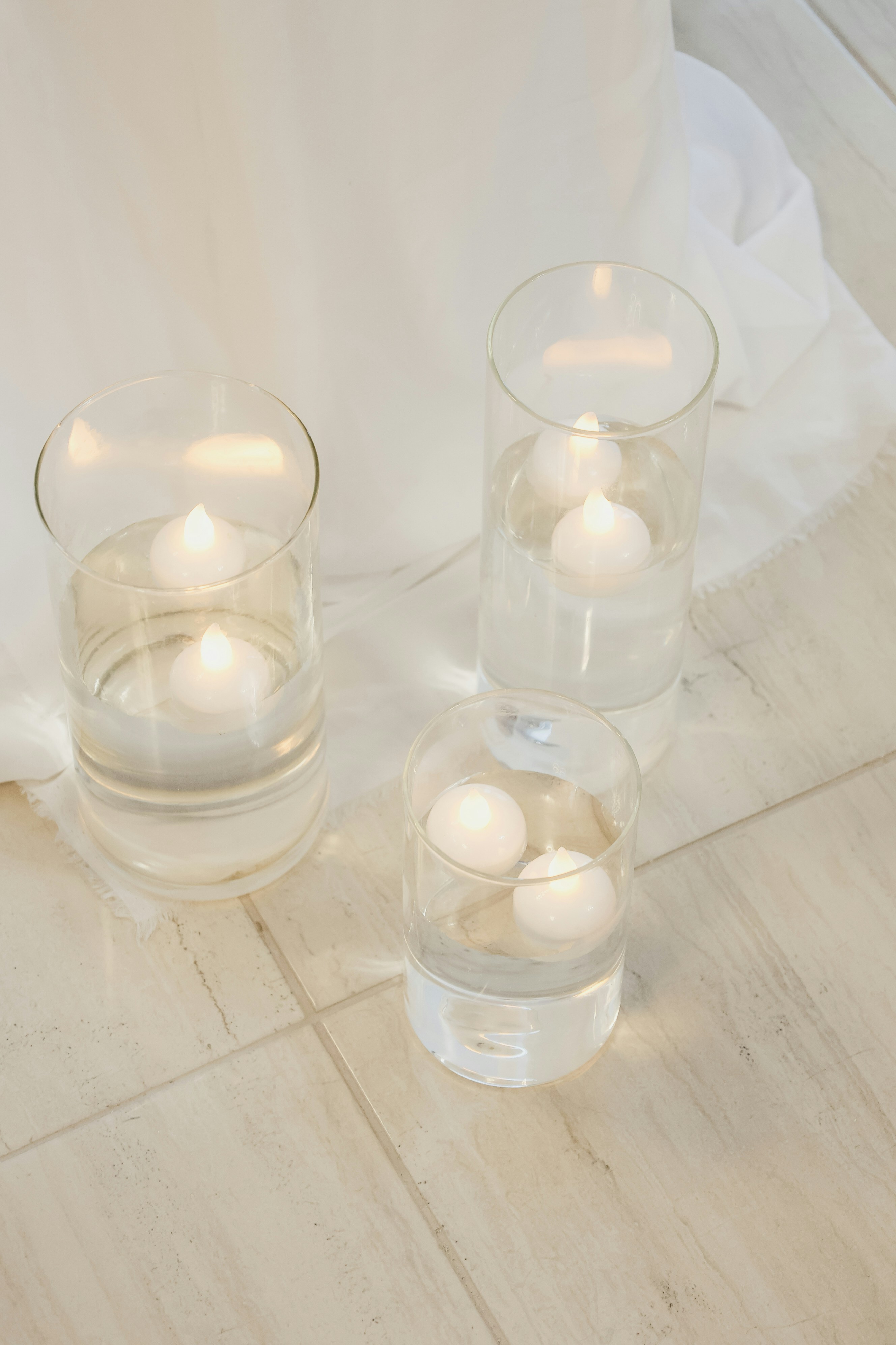 Três vasos de vidro com velas flutuantes e água.
