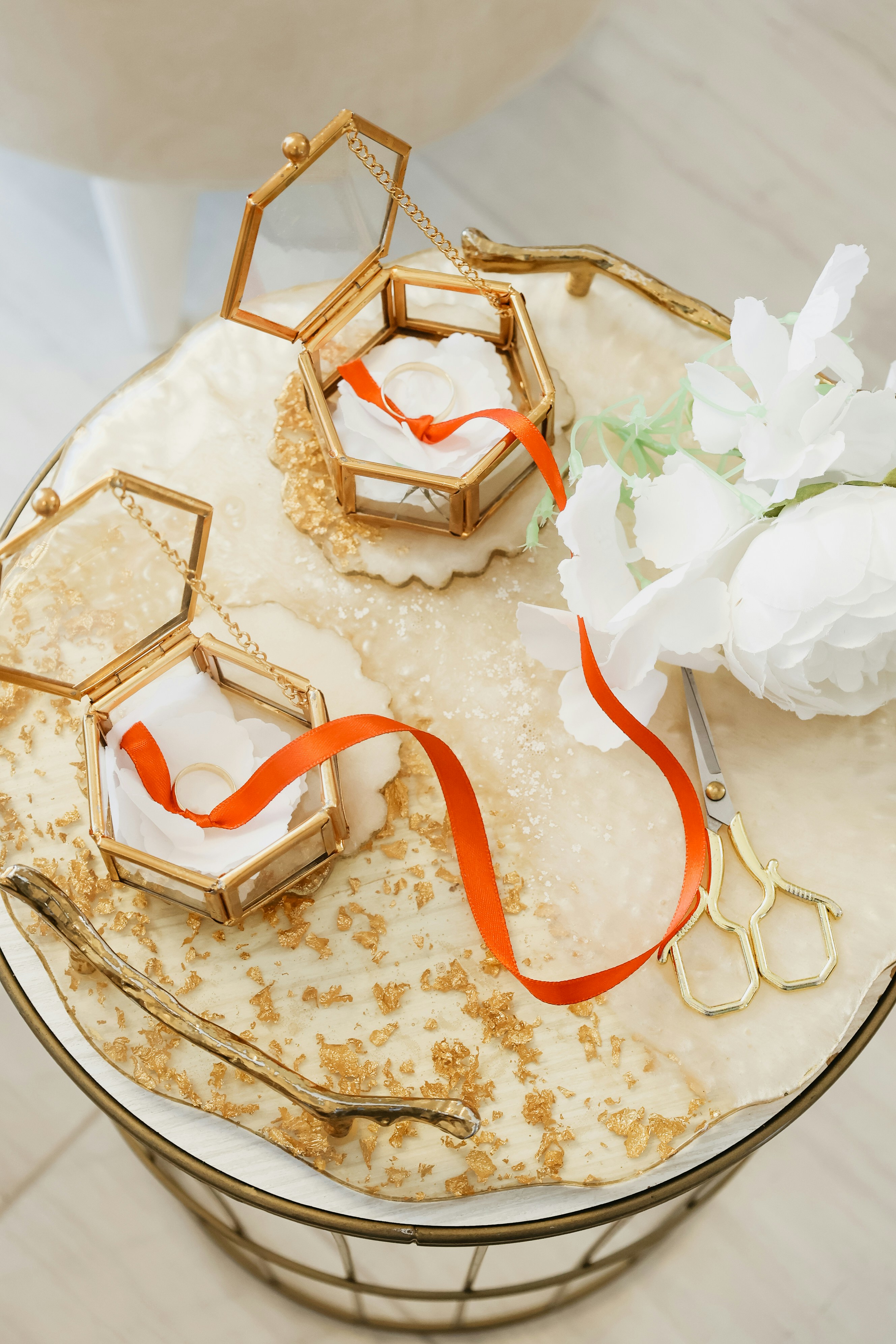 Two wedding rings in hexagonal boxes with orange ribbons.