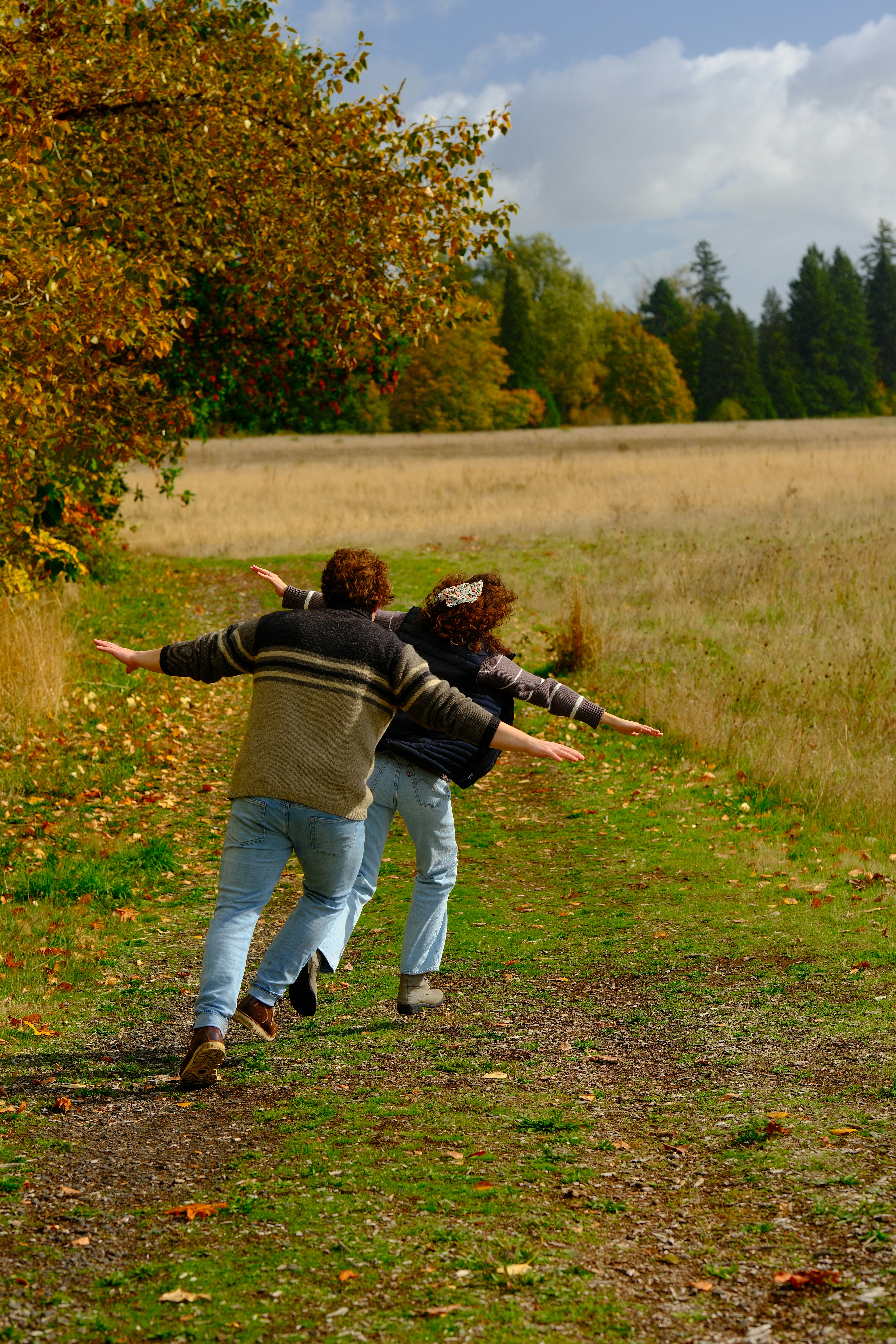 Two people running down a grassy path with arms outstretched.