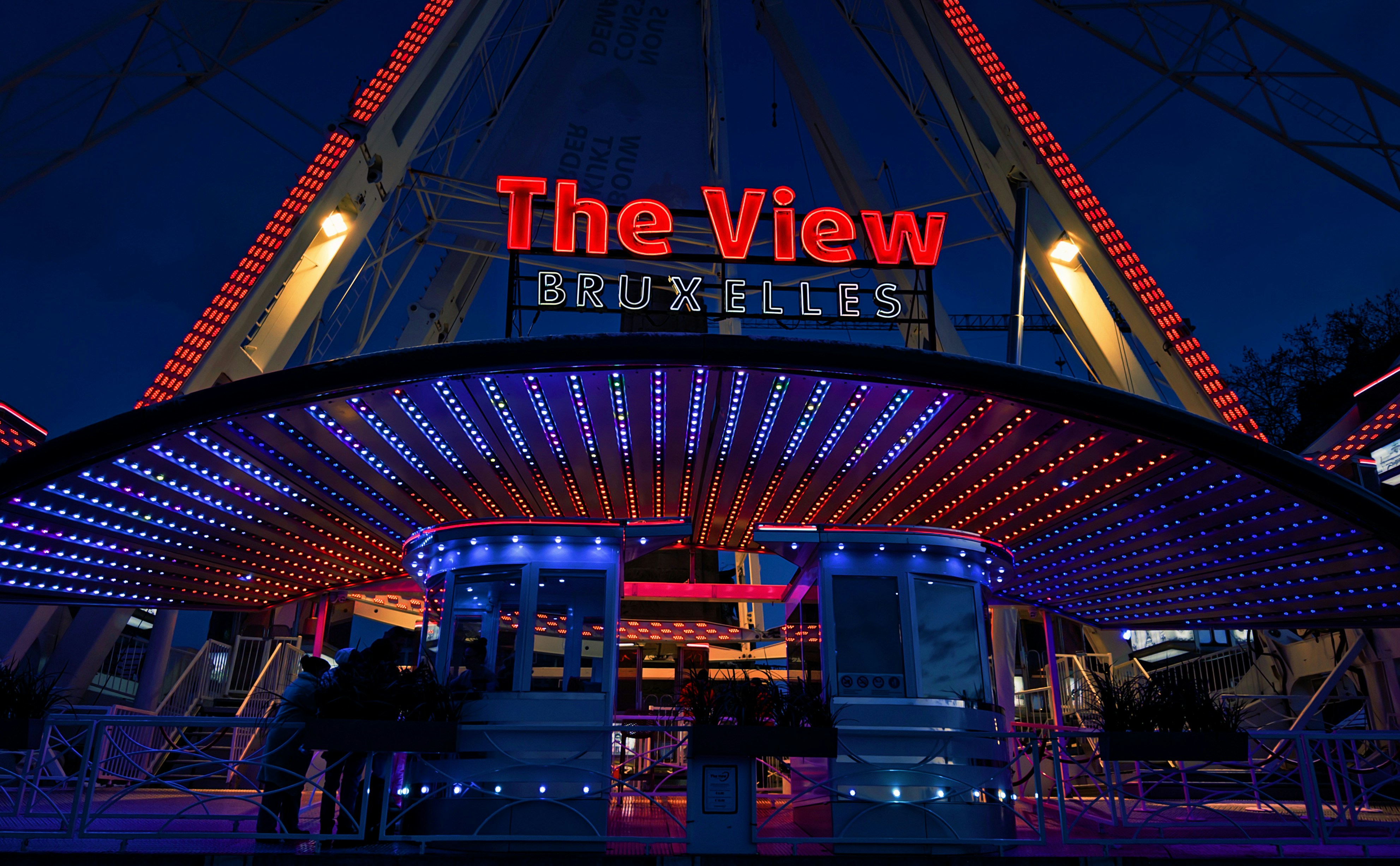 Ferris wheel entrance at night with "the view bruxelles" sign.