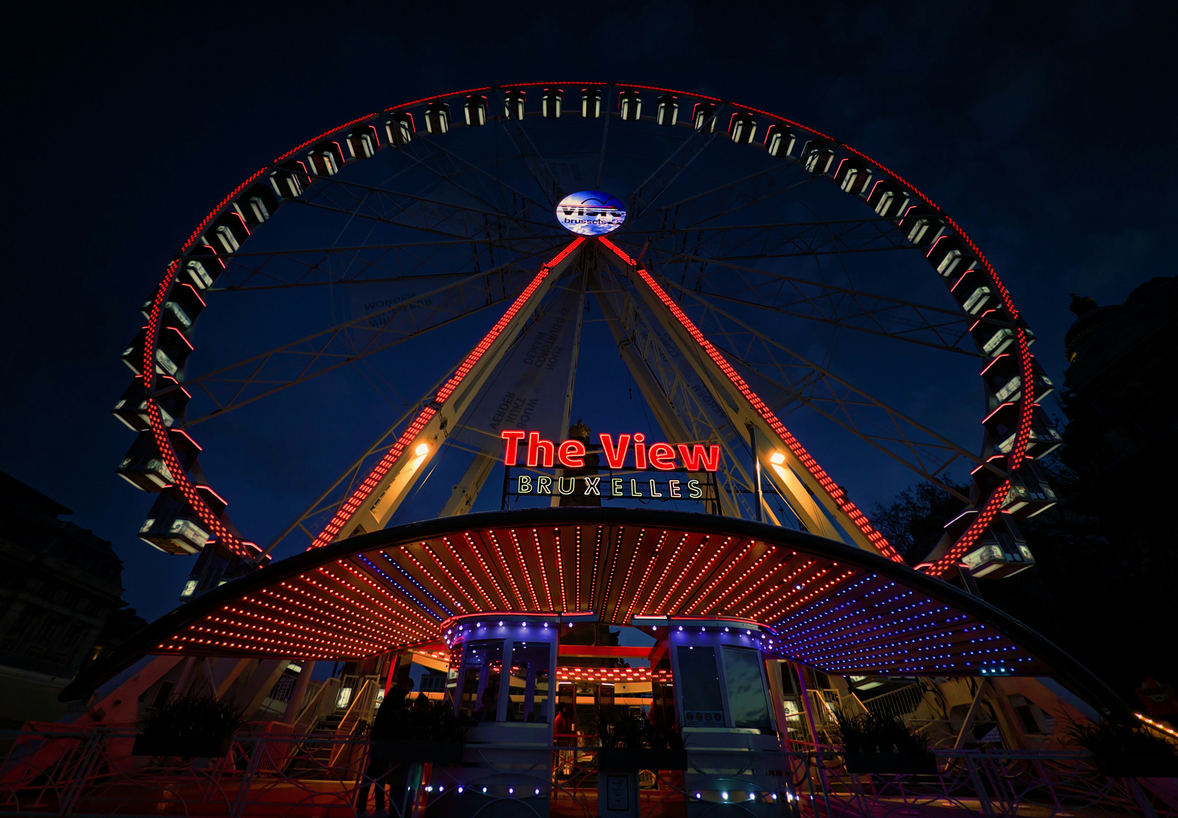 Ferris wheel illuminated at night with "the view bruxelles" sign.
