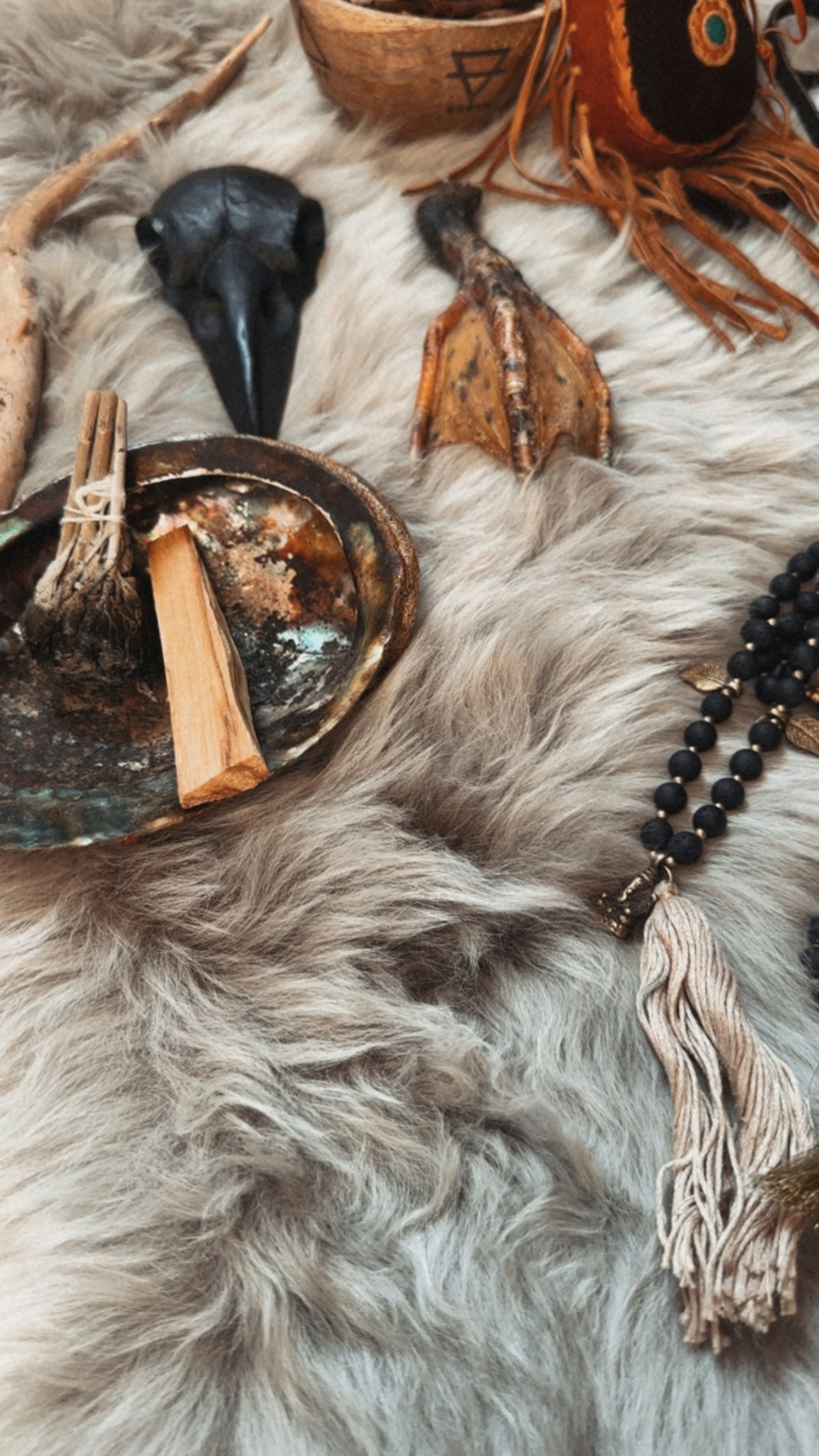 Spiritual objects (sage, palo santo, mala beads) arranged on a textured furry surface, sacred-space still life
