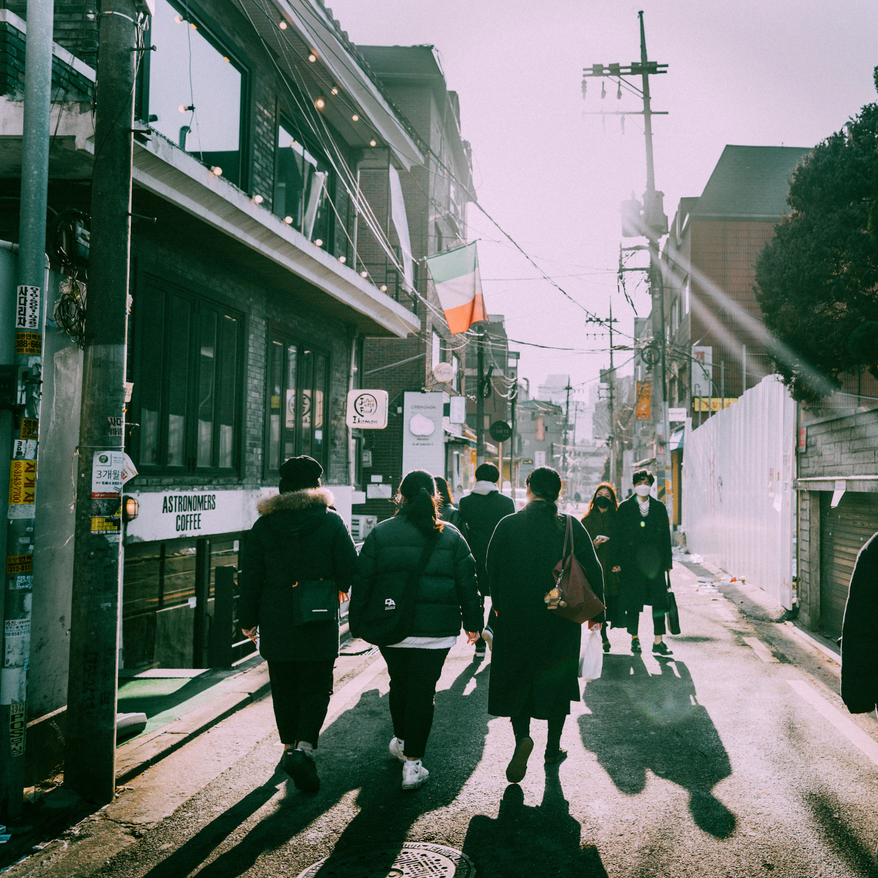 People walk along a narrow city street warmed by low afternoon sunlight.