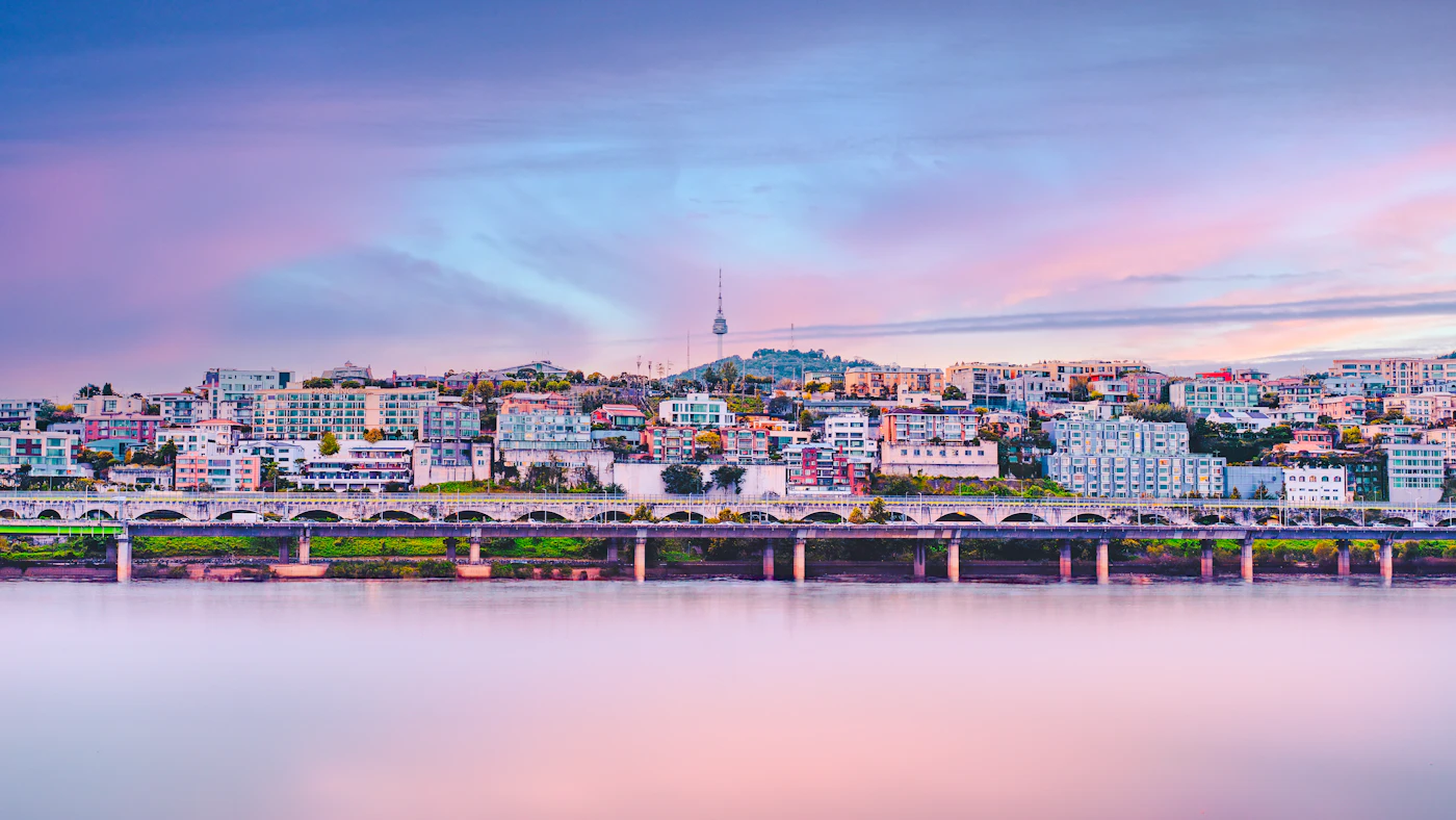 A city skyline with a bridge over a river at dusk