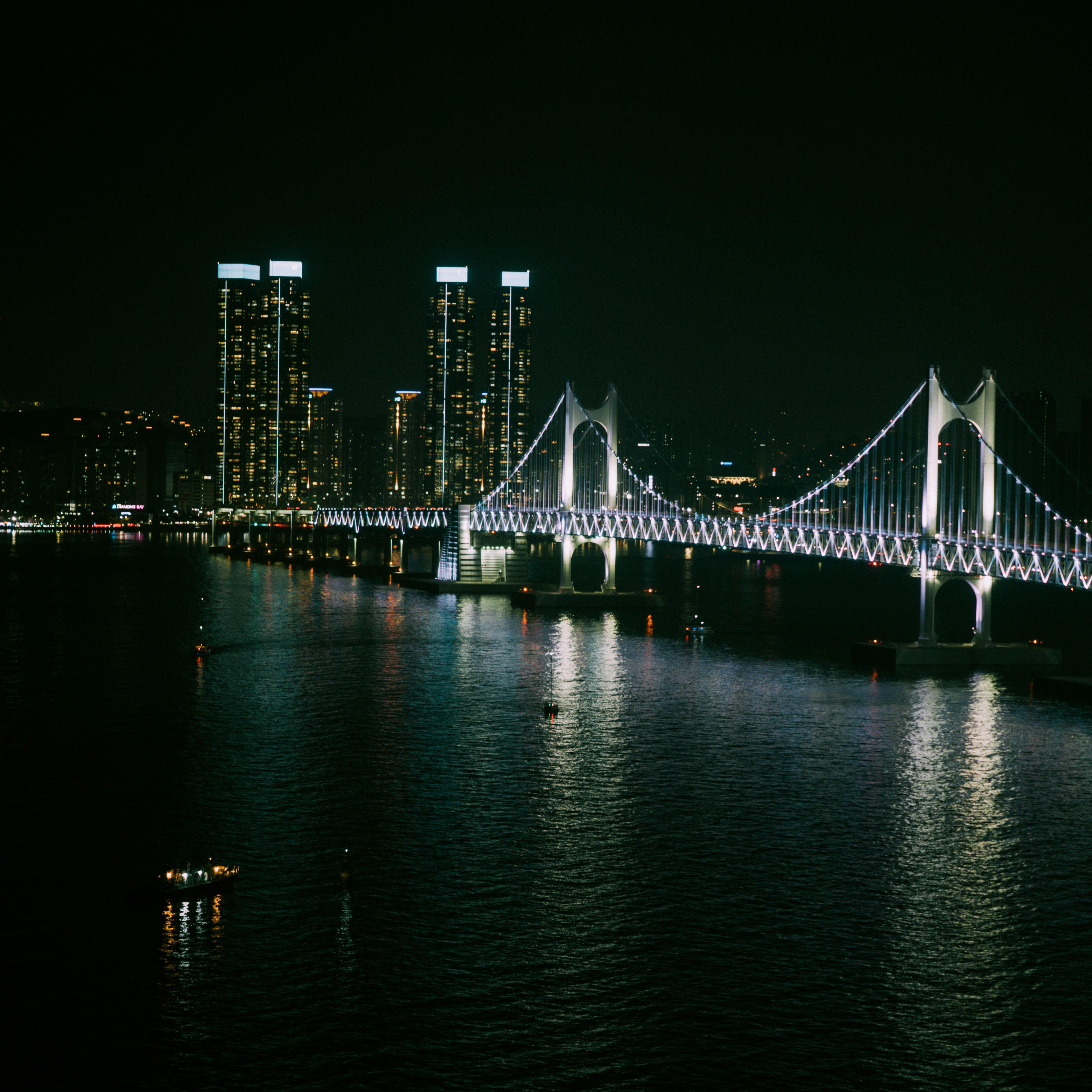 Illuminated suspension bridge over dark water at night.