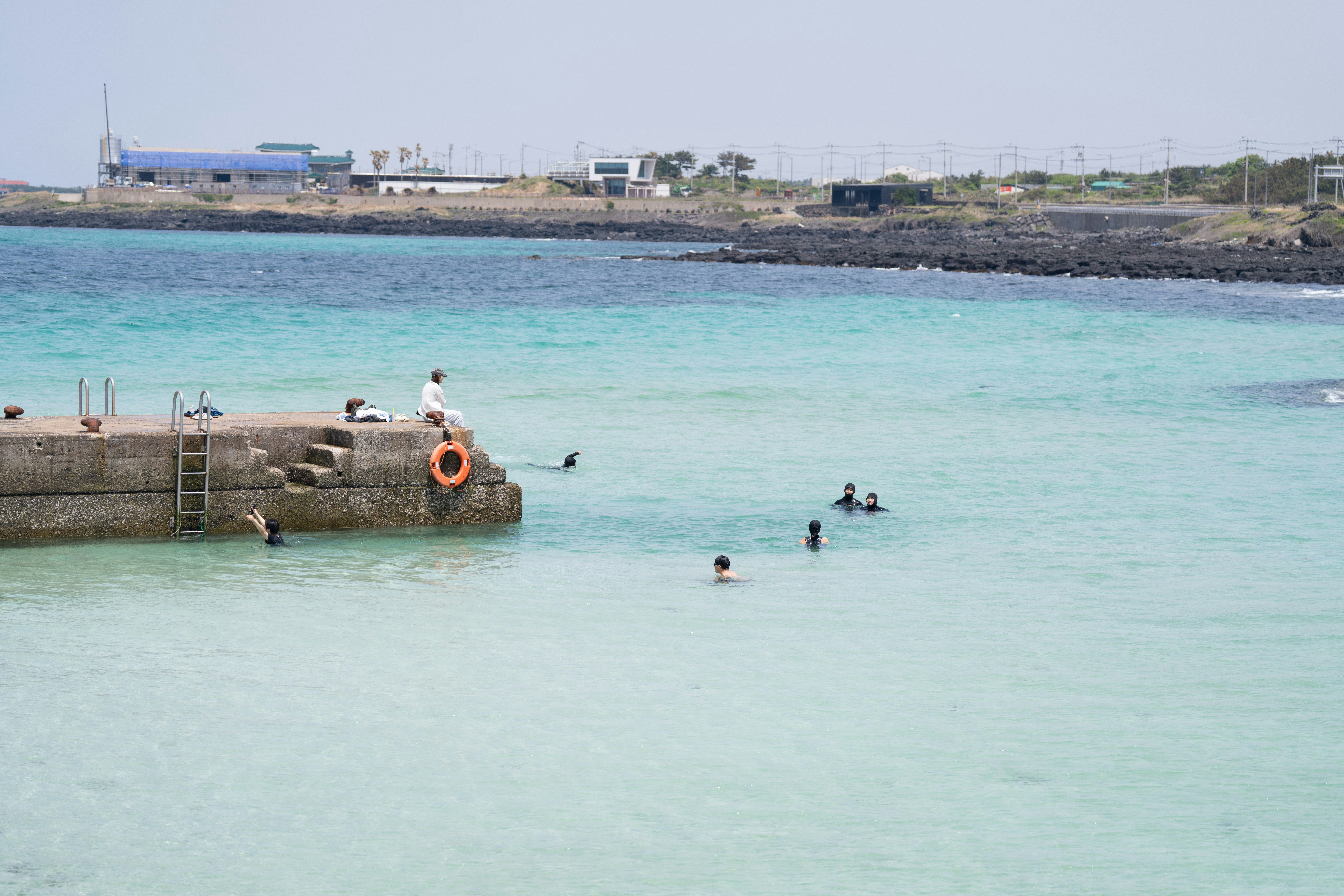 People swimming and relaxing by a concrete pier.