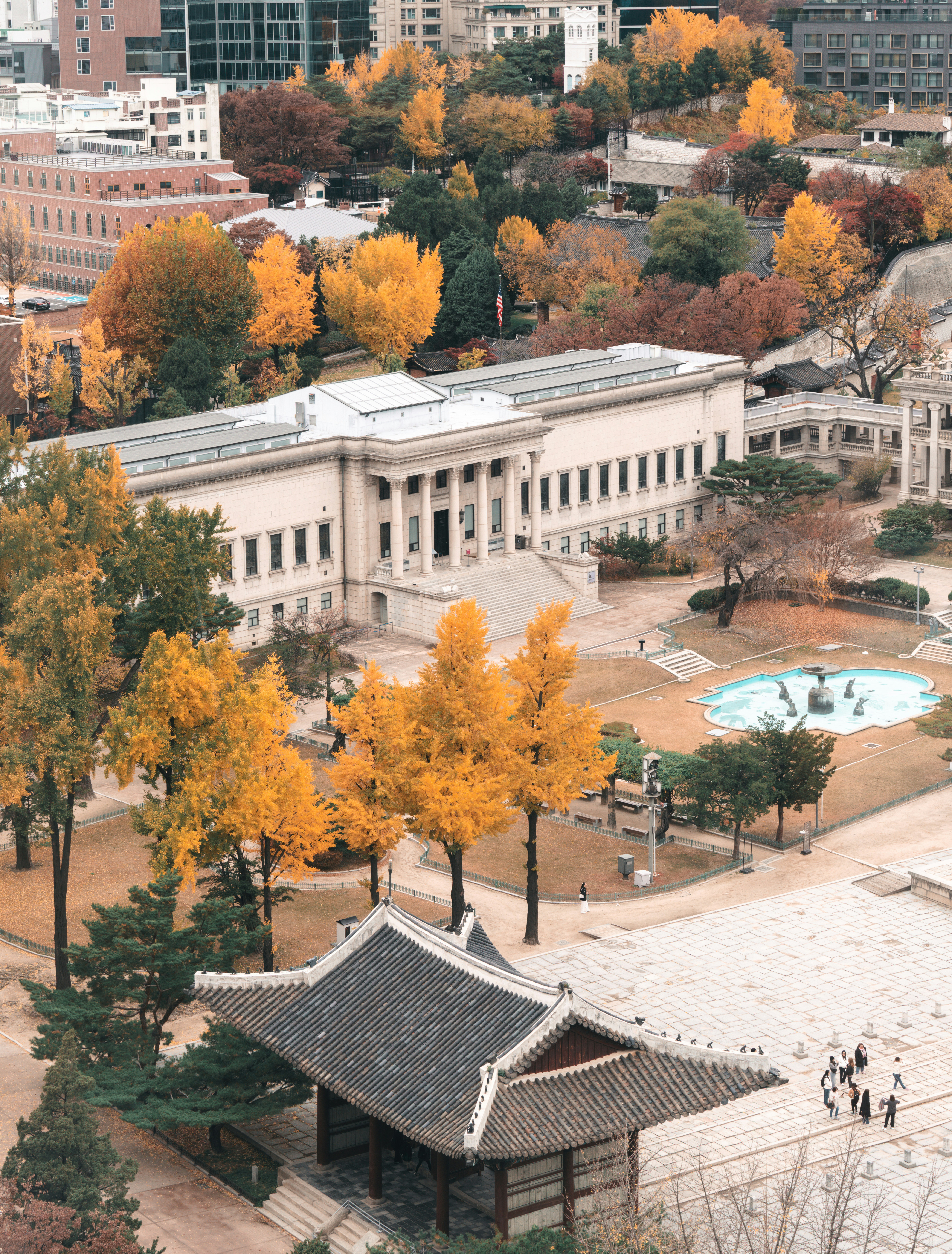 Autumn foliage surrounds a grand building and courtyard.