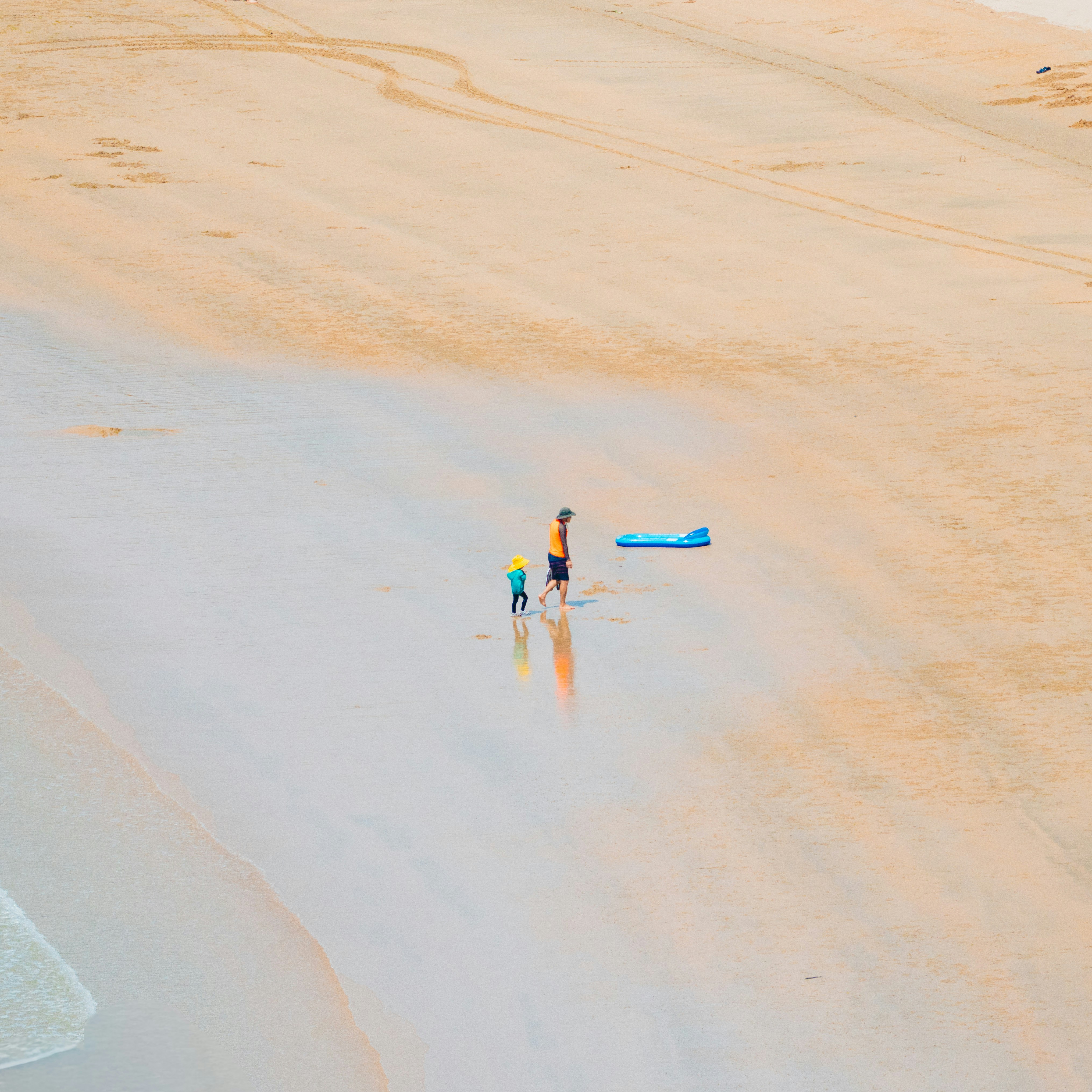 Father and child walk on a wet sandy beach.