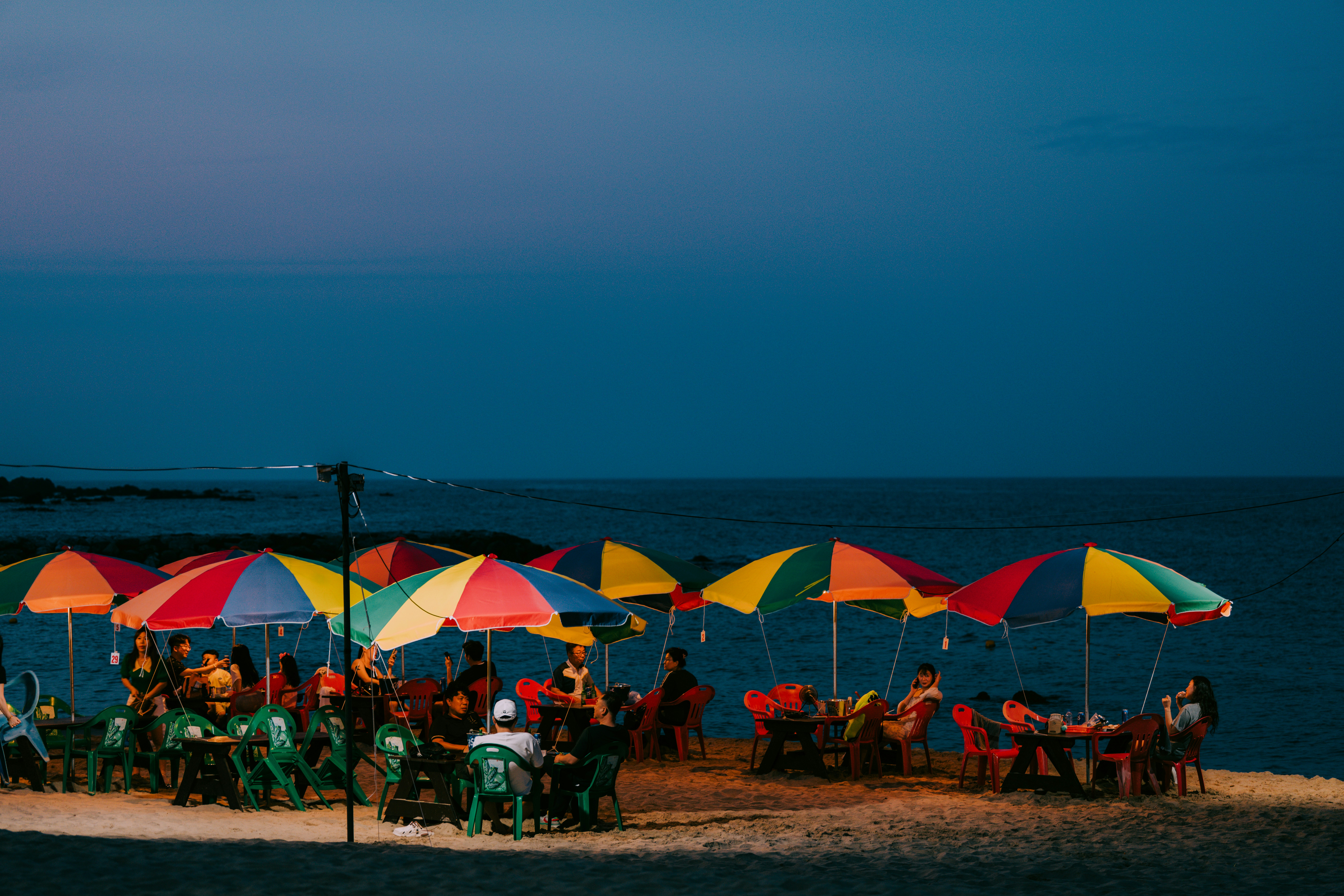 Colorful umbrellas and tables on a beach at dusk.