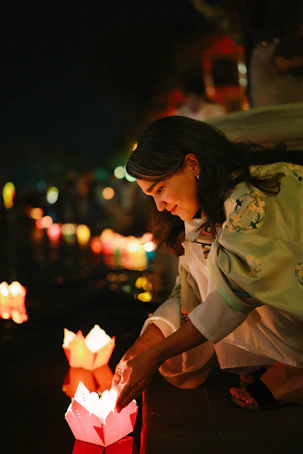 Woman lighting paper lanterns on water at night