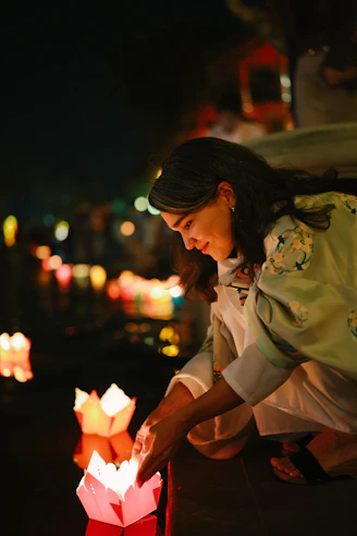 Woman lighting paper lanterns on water at night