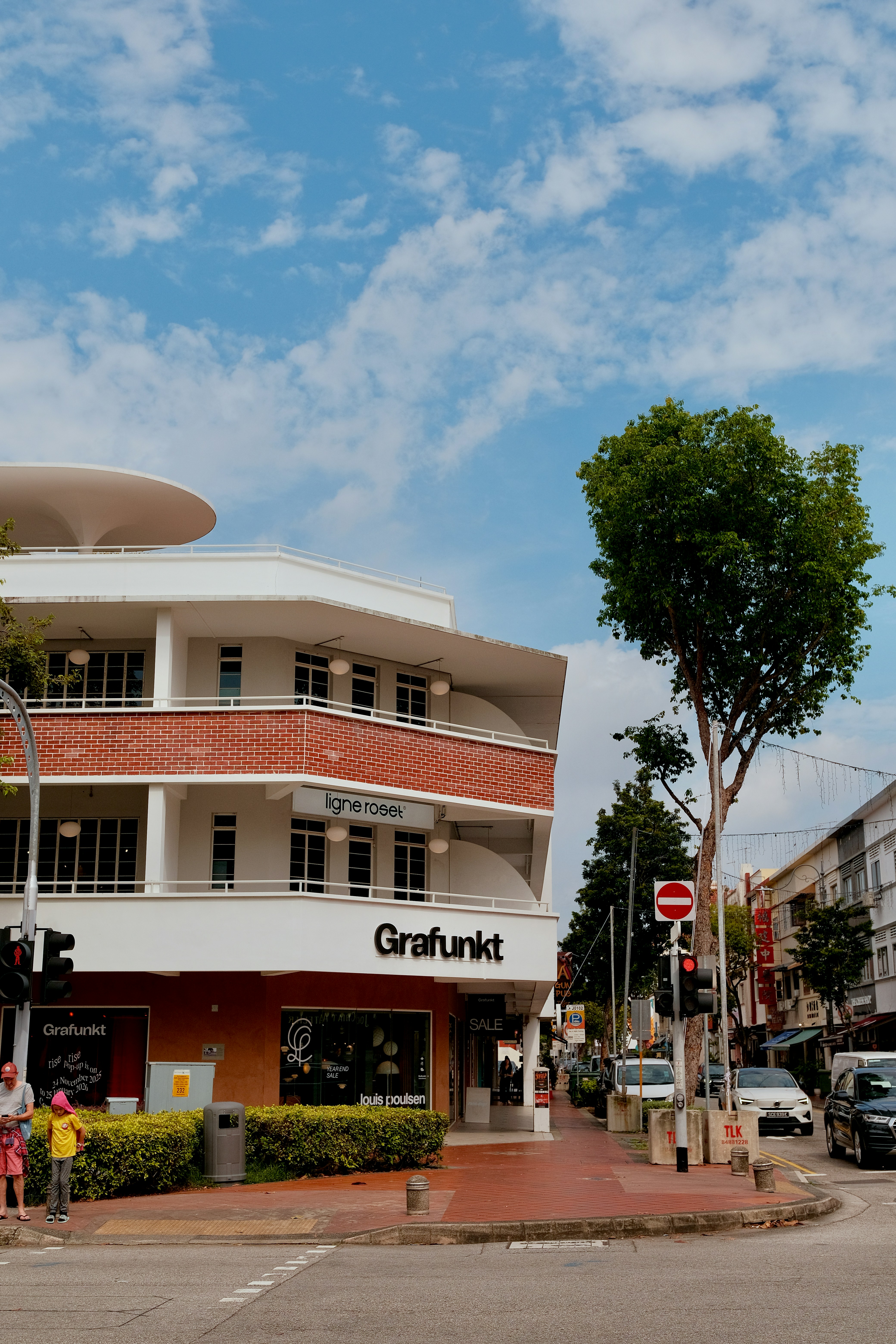 通りに店舗や樹木が並ぶ近代的な建物