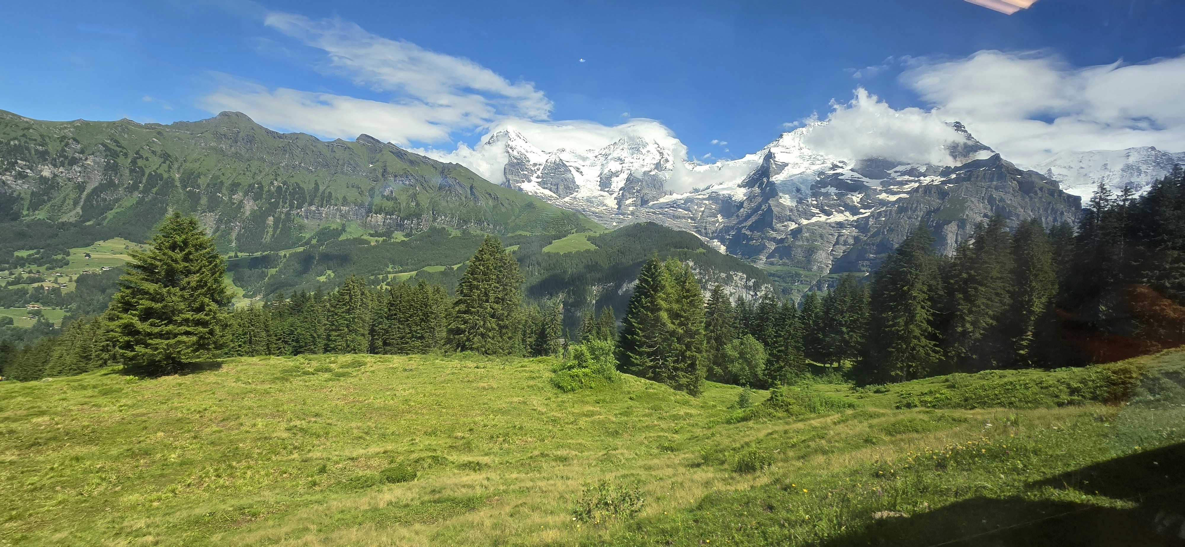 Snow-capped mountains rise above a green, forested valley.