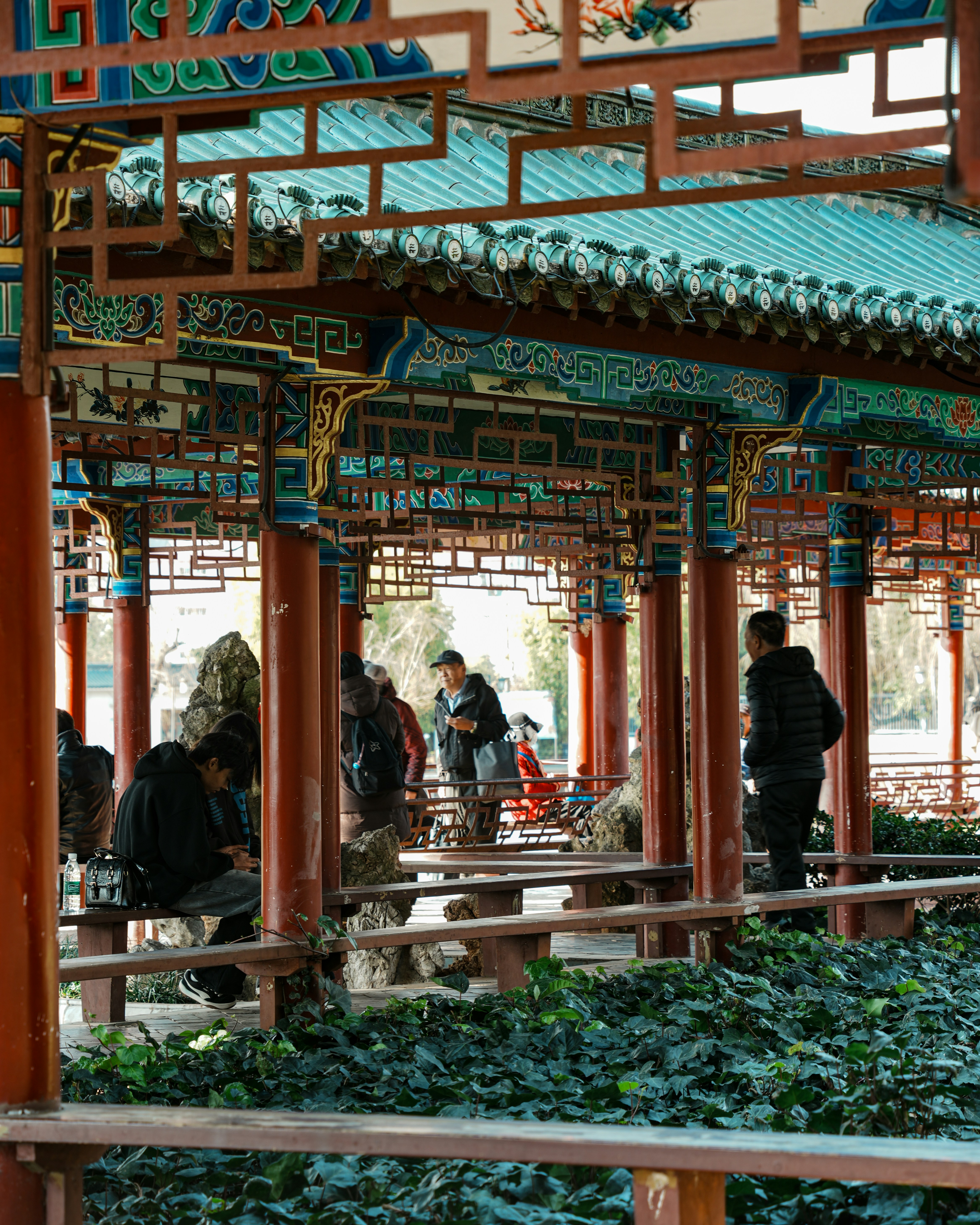 People relax under a colorful ornate chinese pavilion