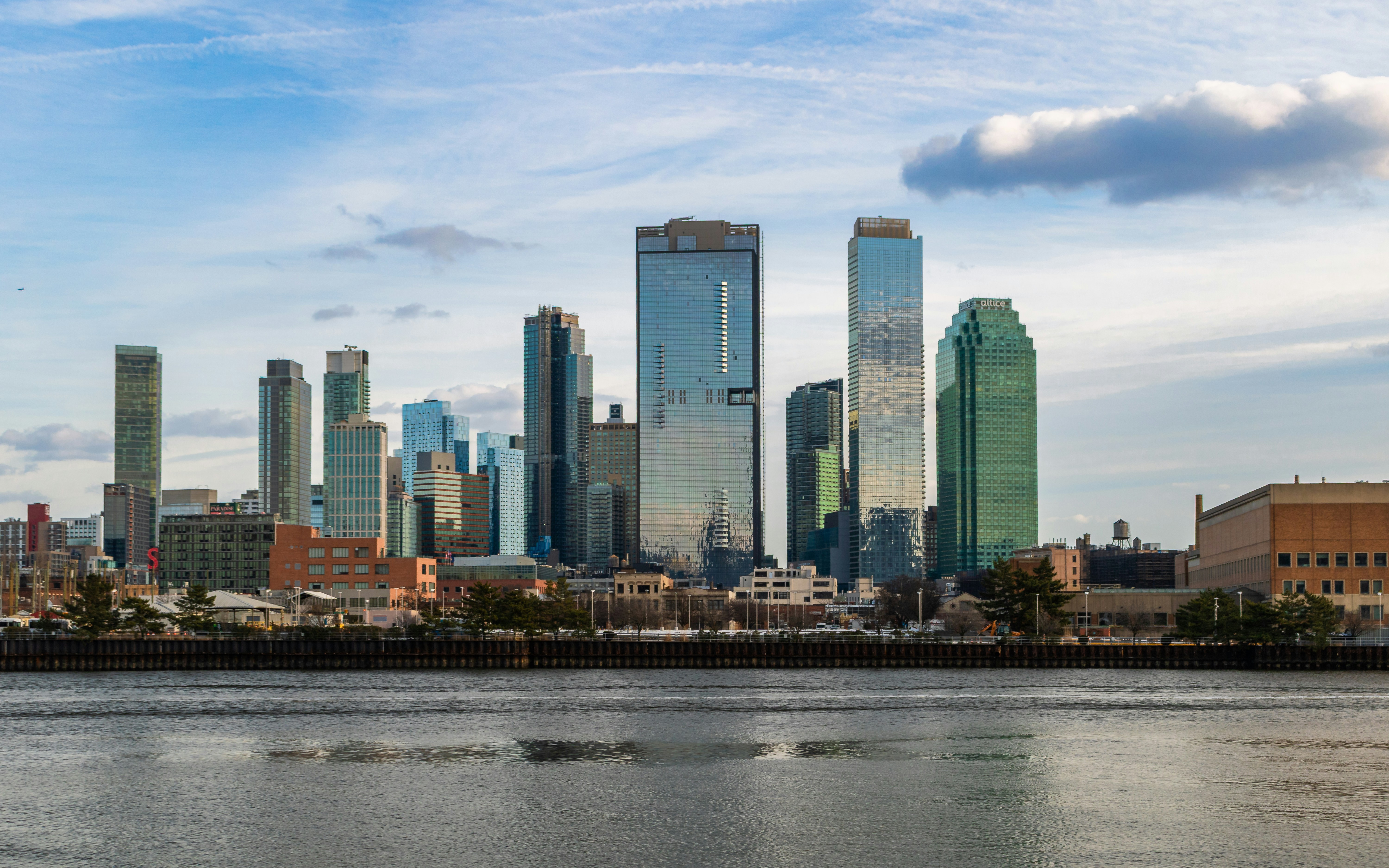 Modern skyscrapers line the waterfront under a cloudy sky.
