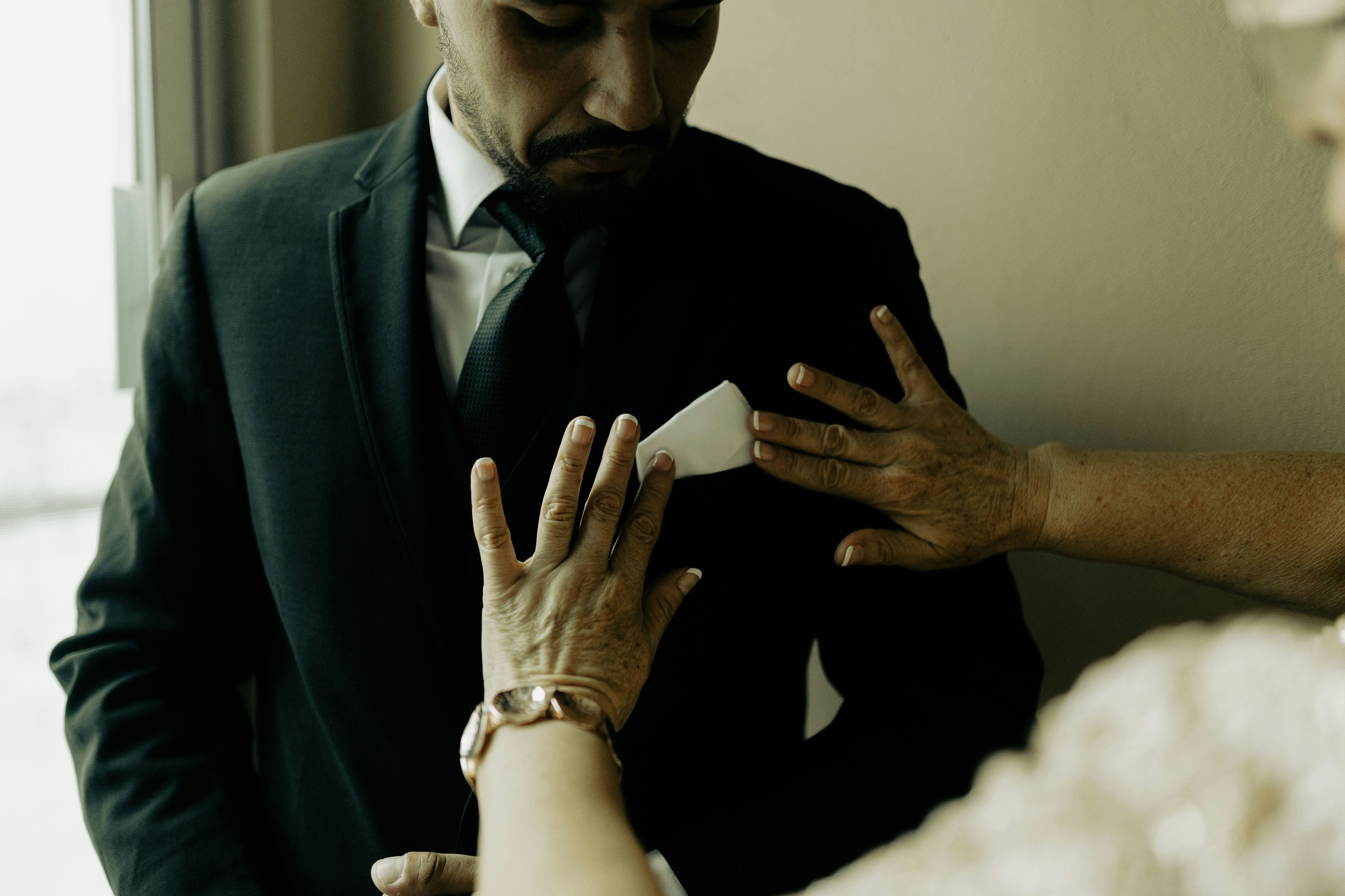 A person adjusts a man's suit pocket square