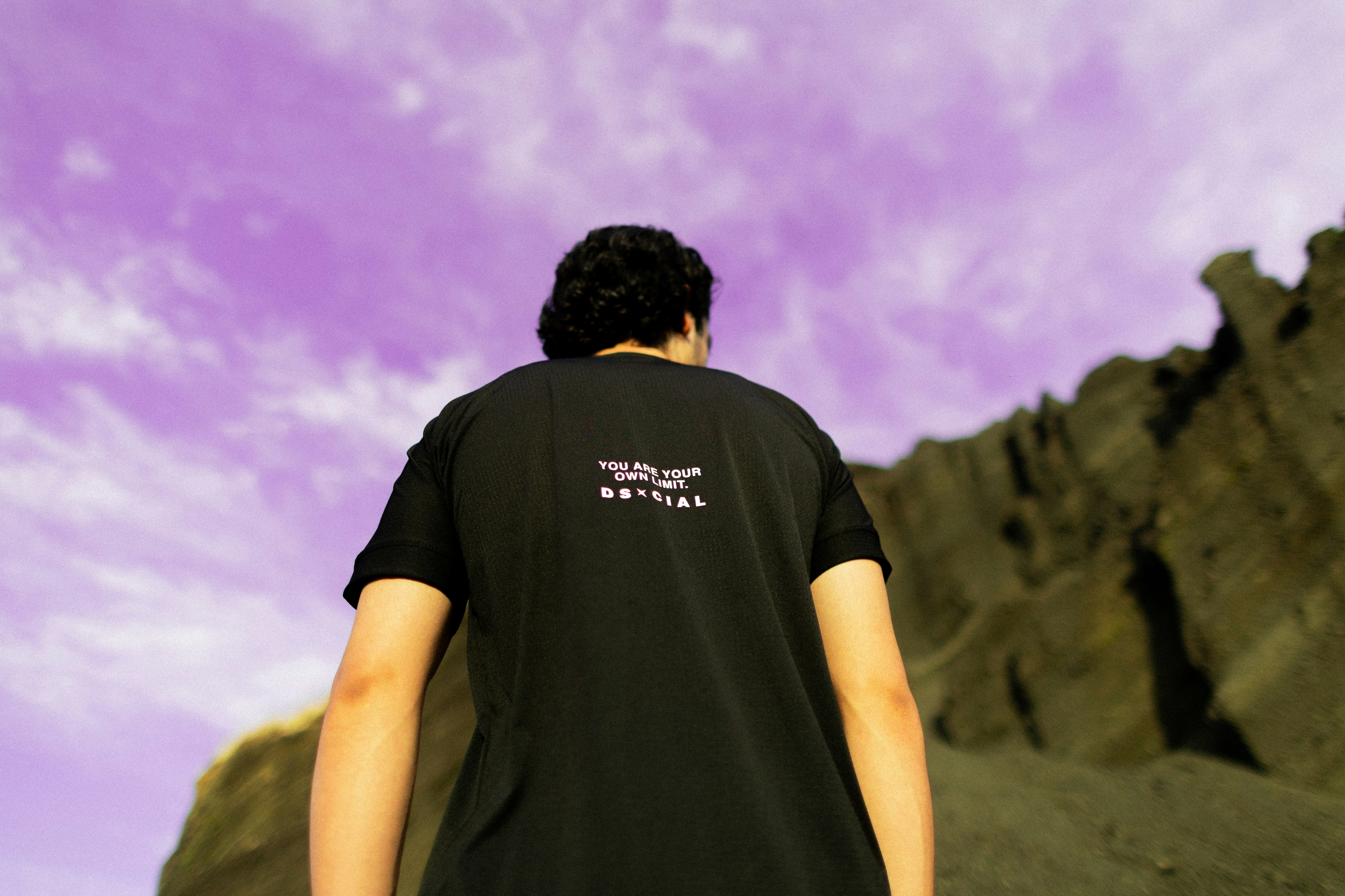 Person wearing black t-shirt against purple sky and rocks