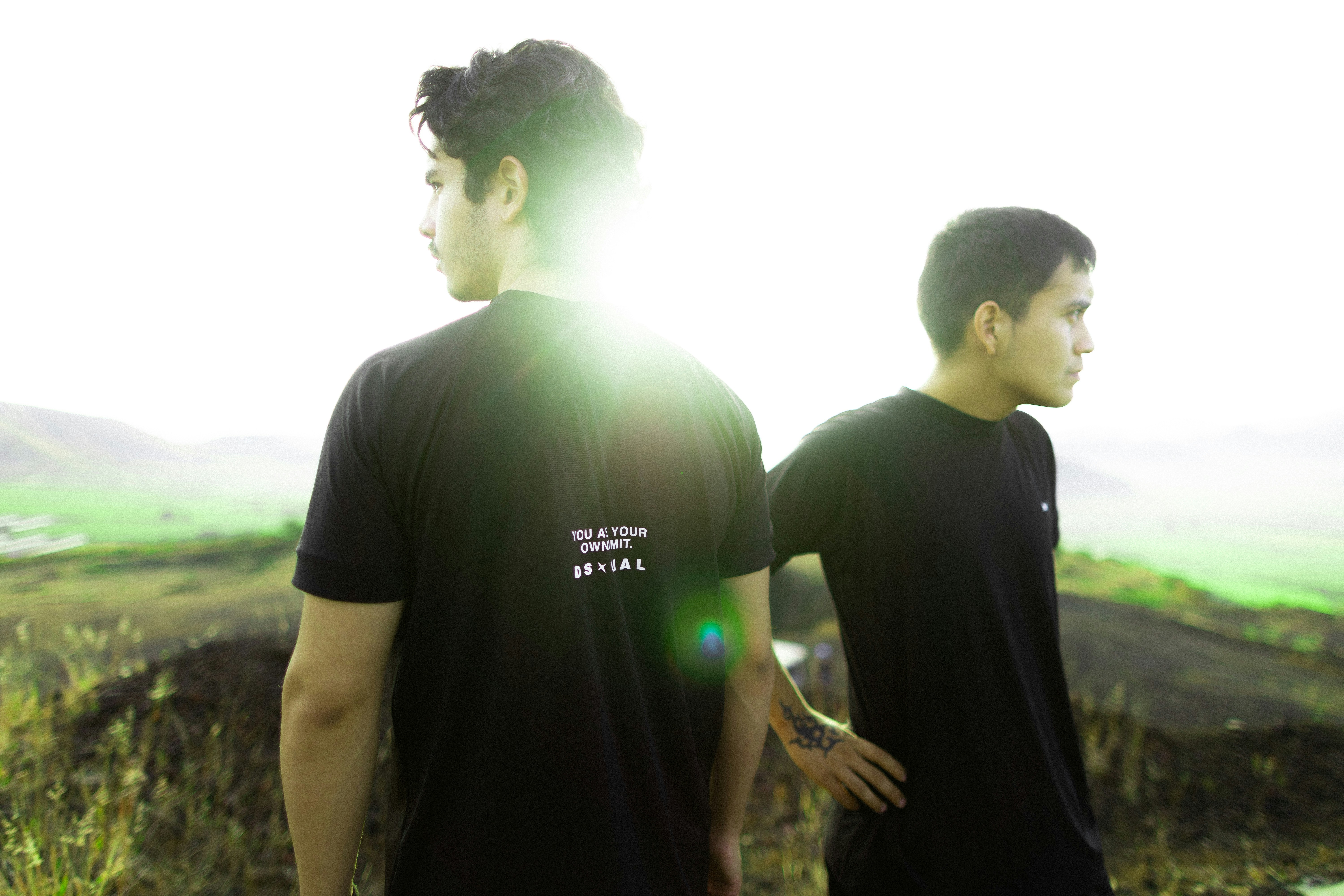 Two young men stand on a hill overlooking a landscape.