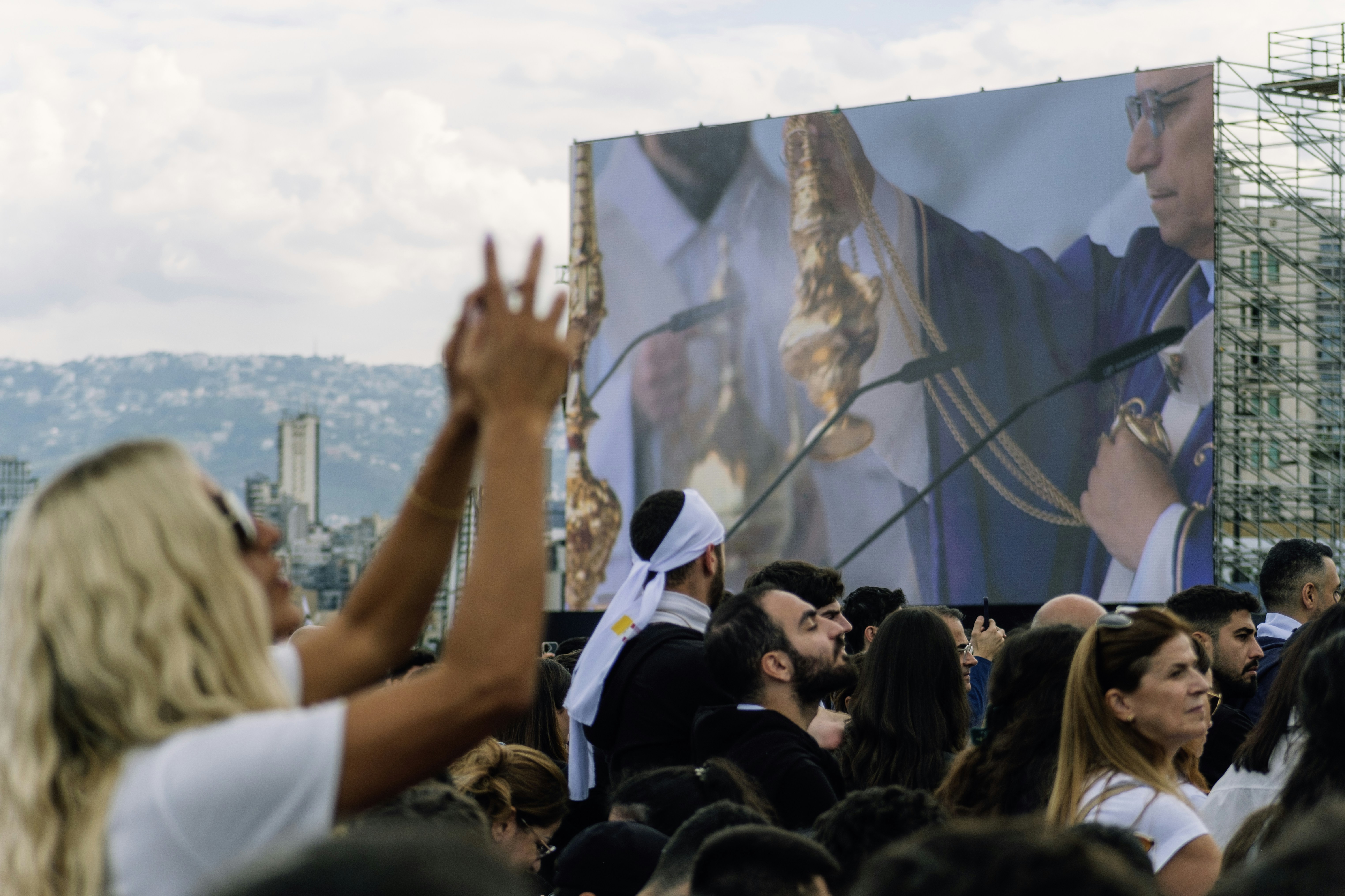 Crowd watches a large screen showing a religious ceremony