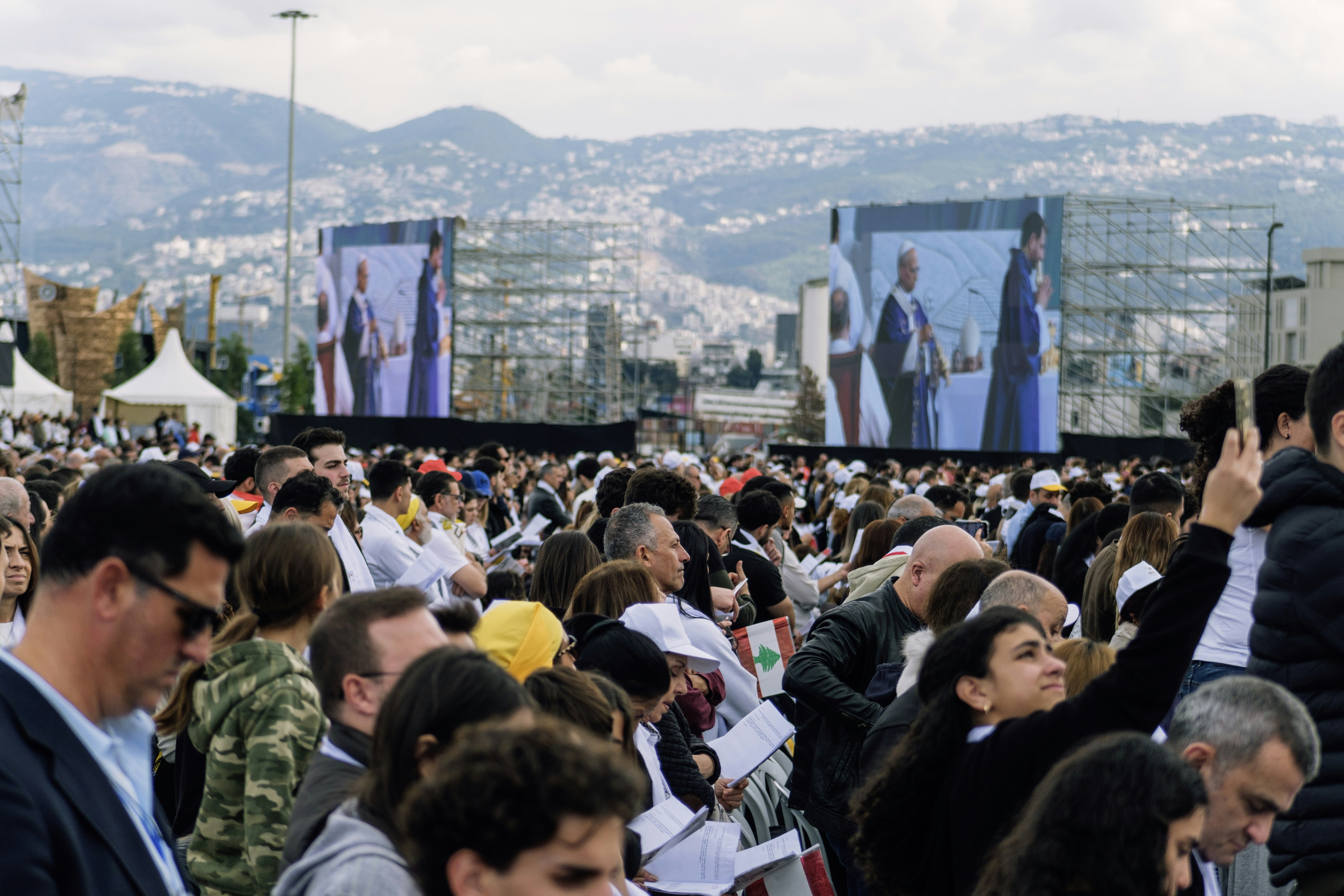 Large crowd watches speakers on large outdoor screens