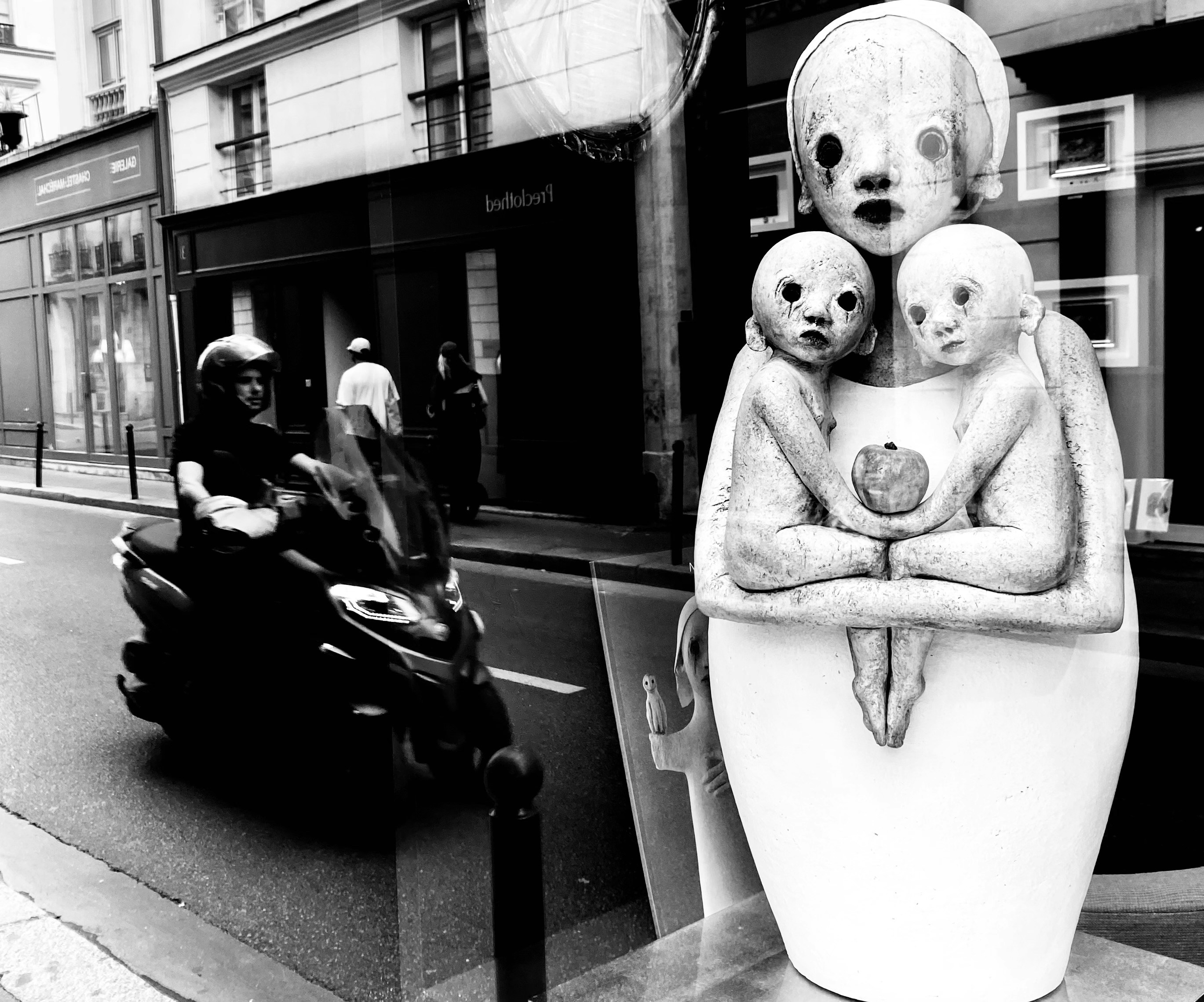 Motorcyclist passes a surreal sculpture on street.