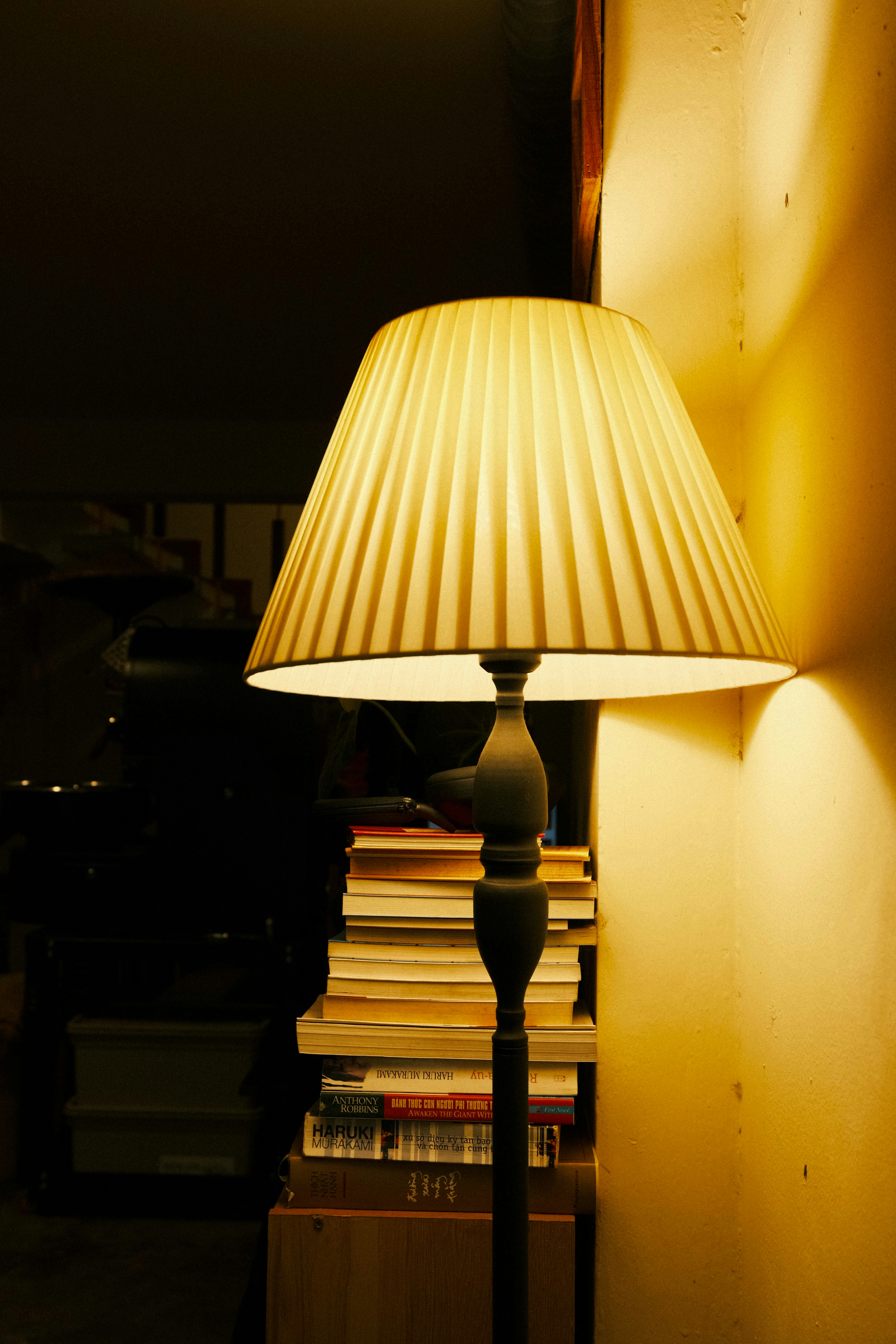 A lit lamp stands beside a stack of books.