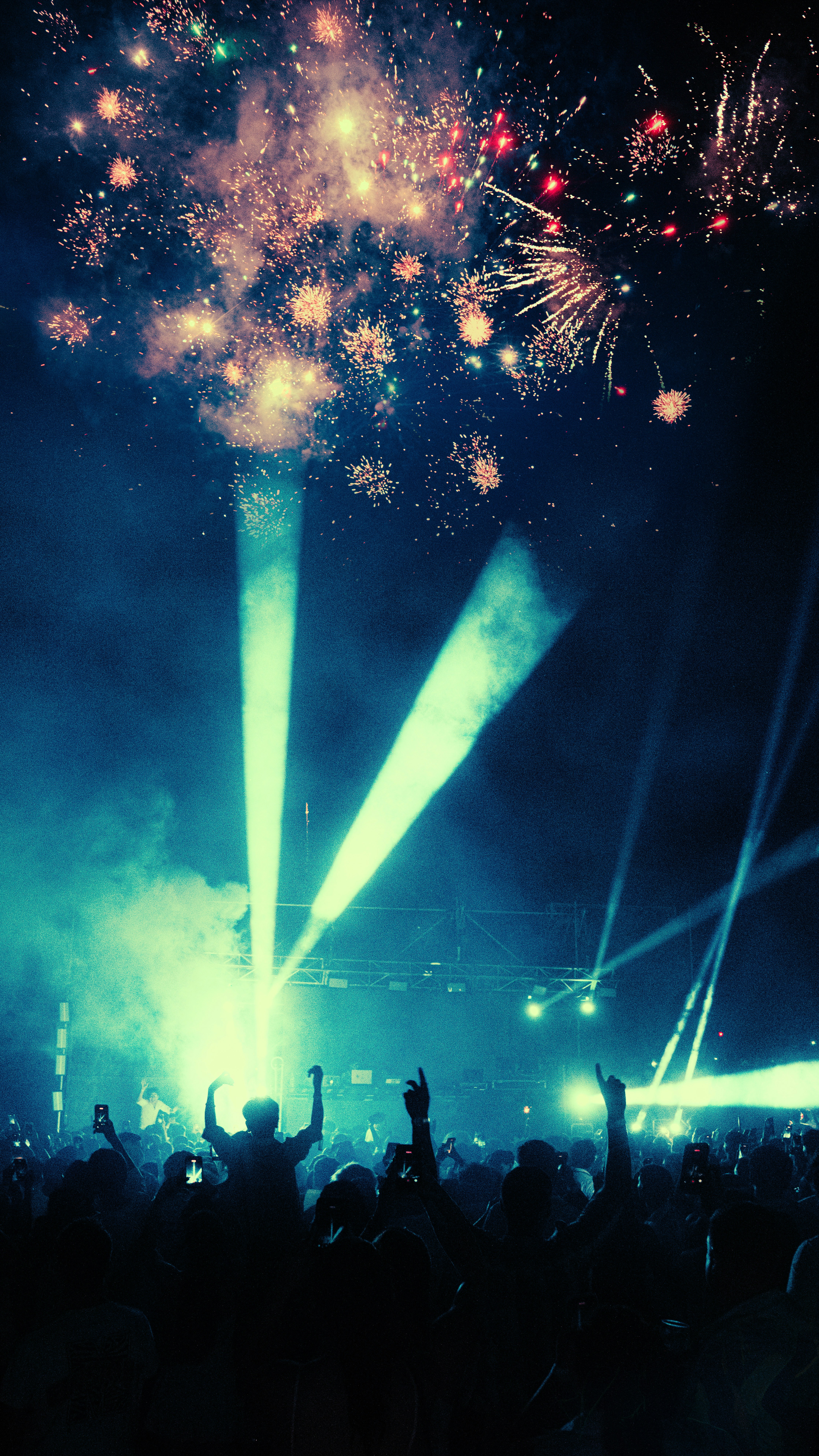 Fireworks explode over a cheering crowd at a concert.