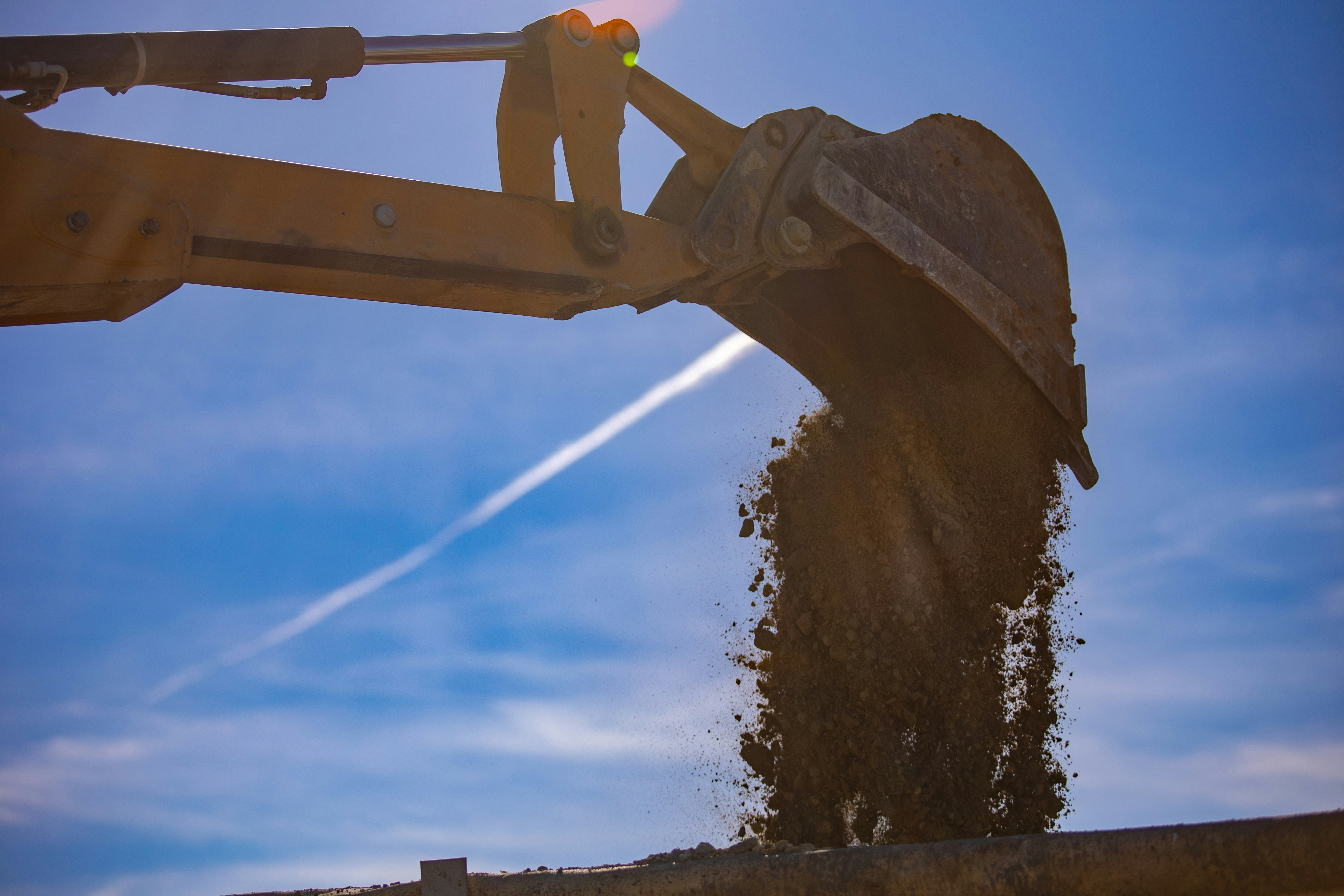 Excavator bucket dumping dirt against a blue sky