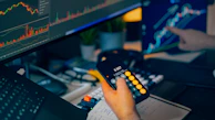Trader analyzing stock market charts on computer screens with calculator.