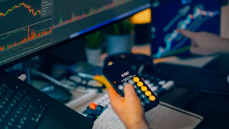 Trader analyzing stock market charts on computer screens with calculator.