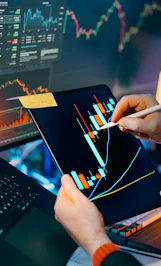 Trader analyzing stock market charts on tablet and monitor
