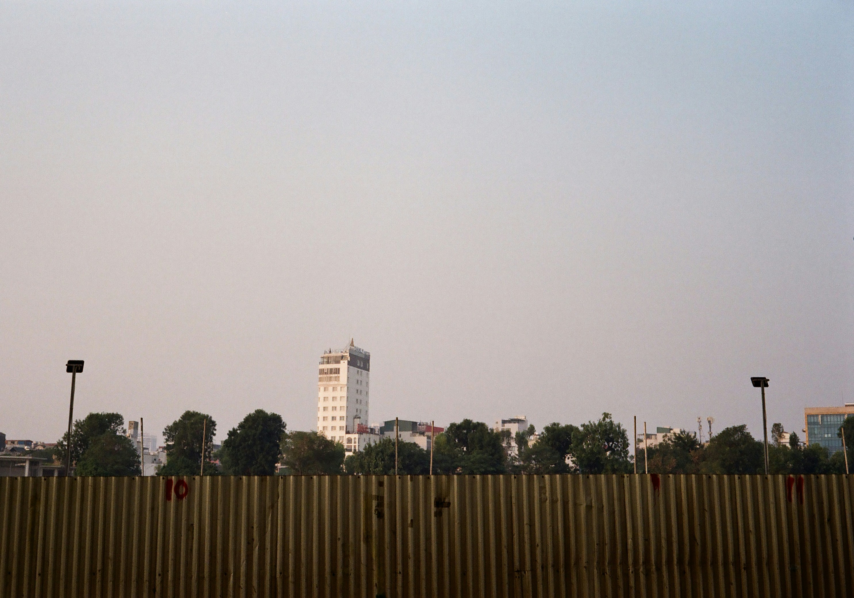 Tall building behind trees and yellow fence