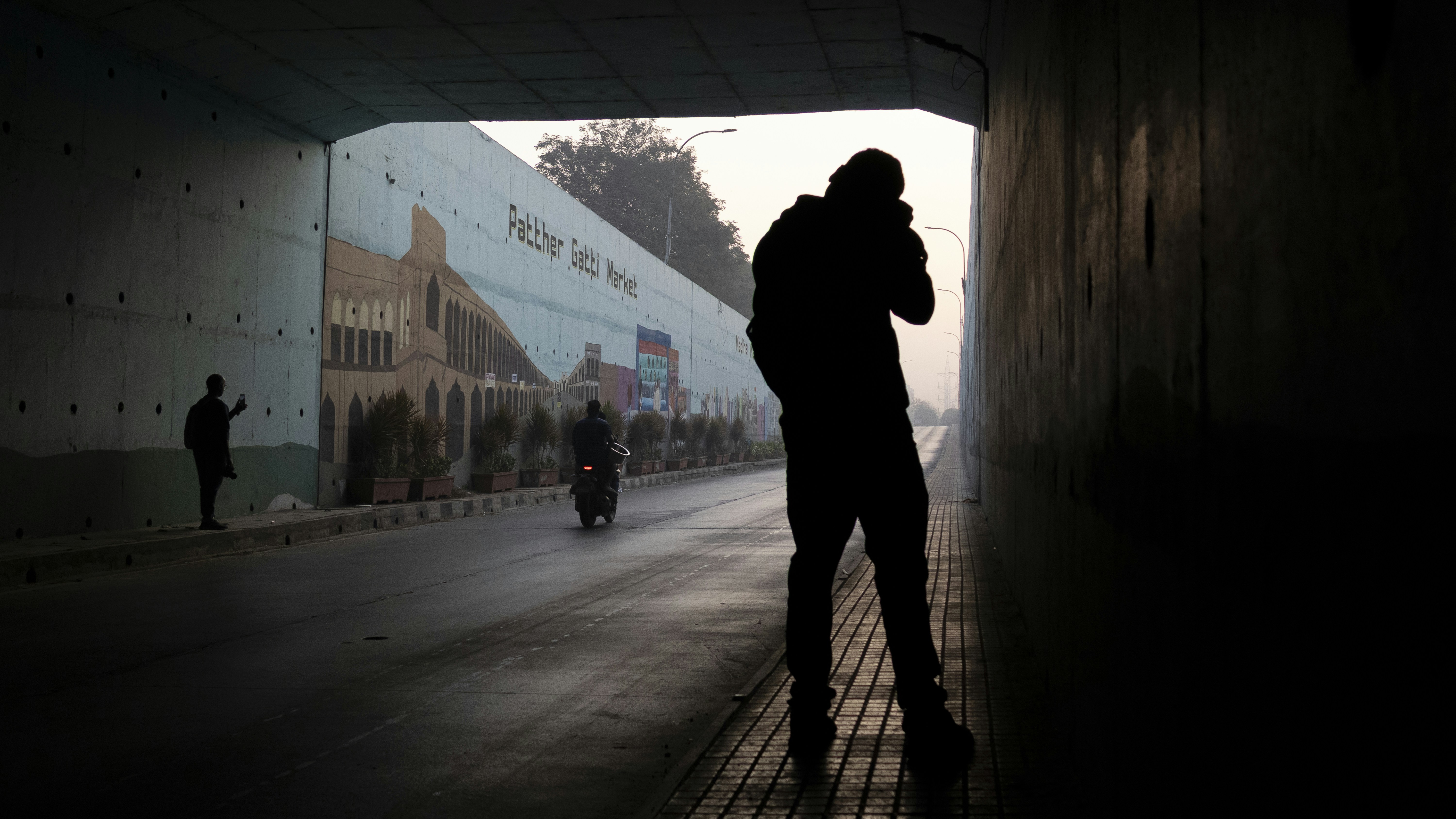Man silhouetted in a dark tunnel with mural on wall.