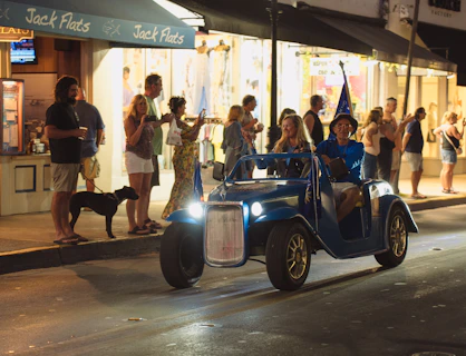Man in wizard hat drives blue car at night.
