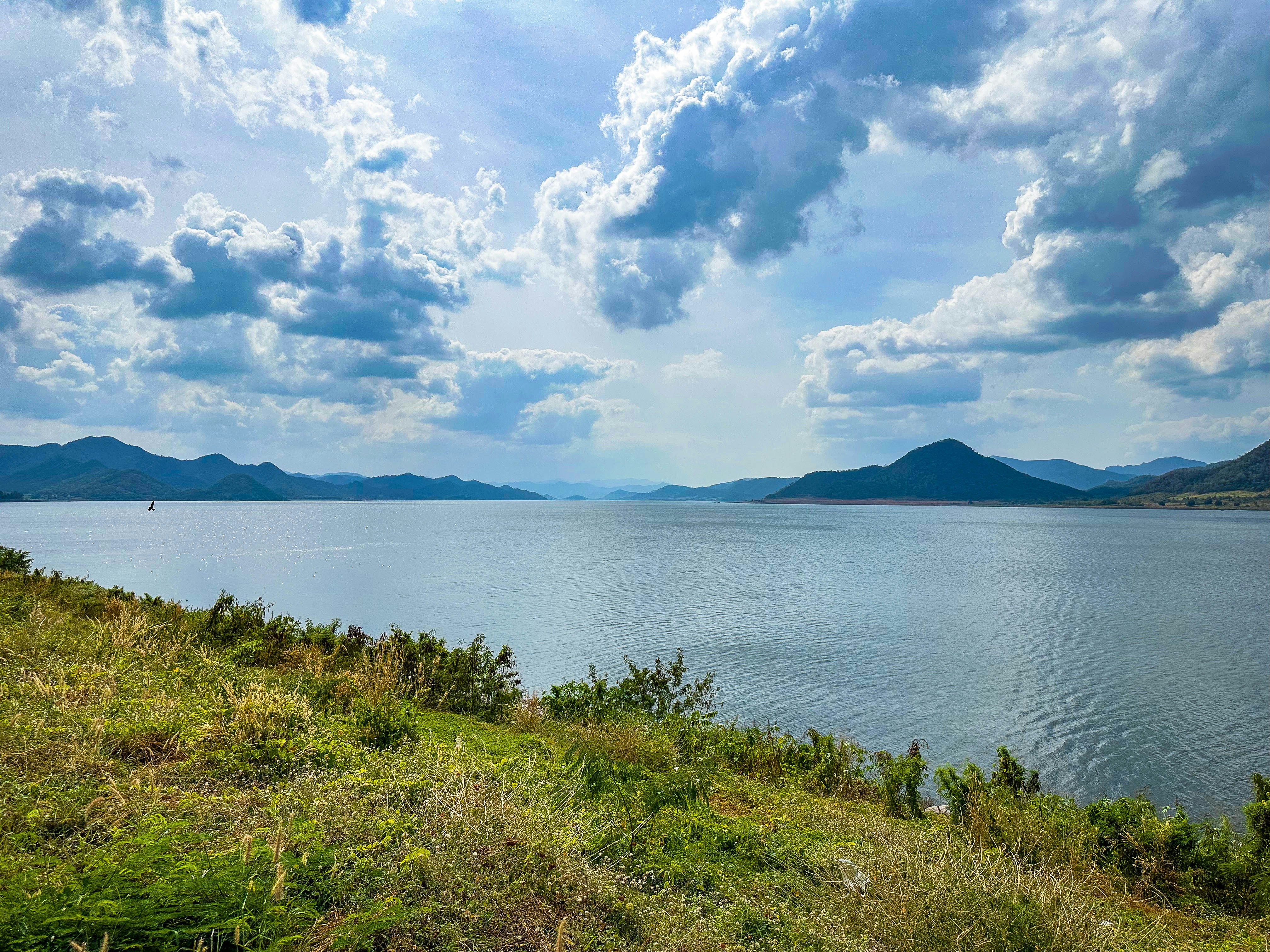 Lago calmo cercado por colinas onduladas sob céu nublado