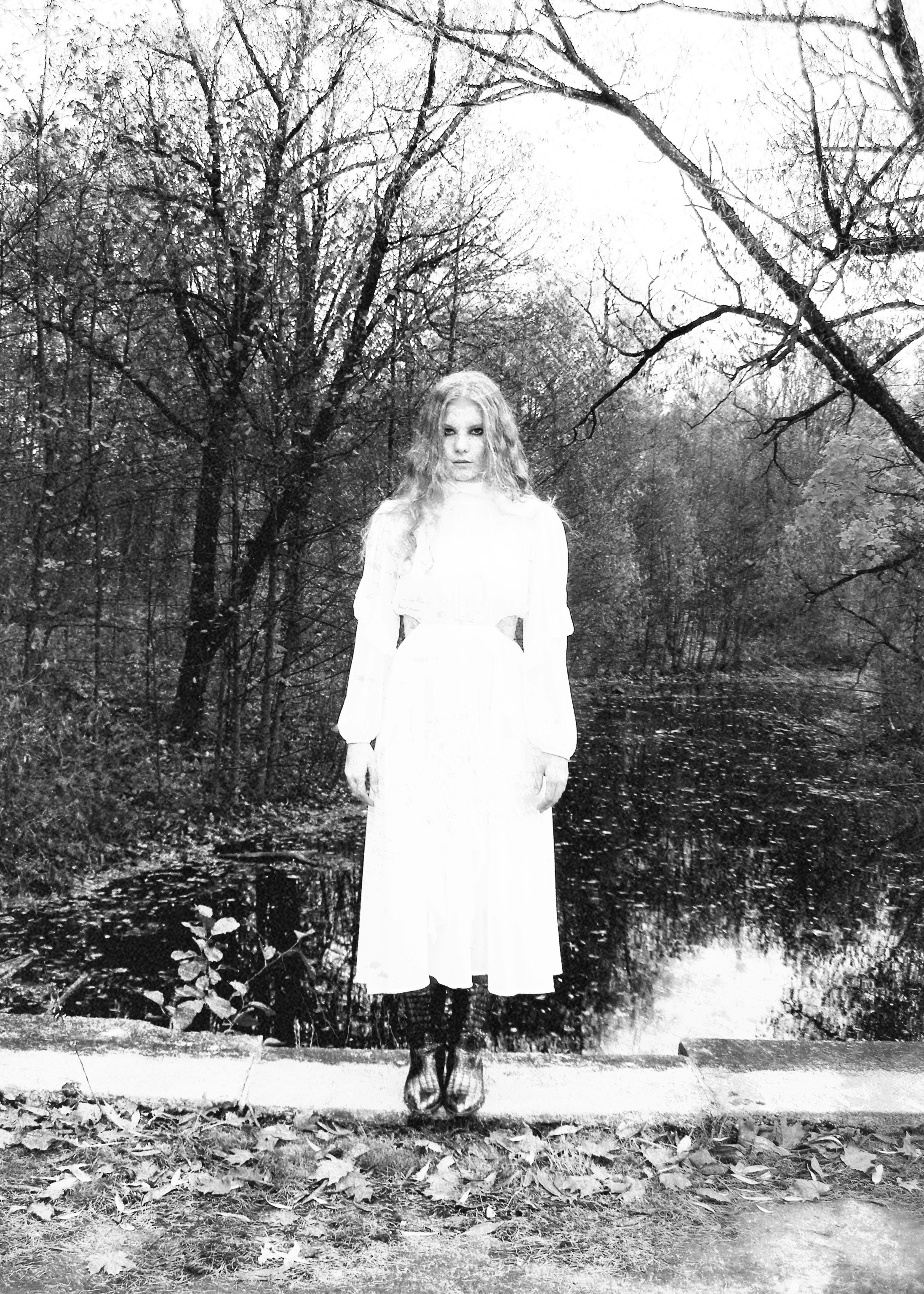 Woman in white dress standing in a spooky forest