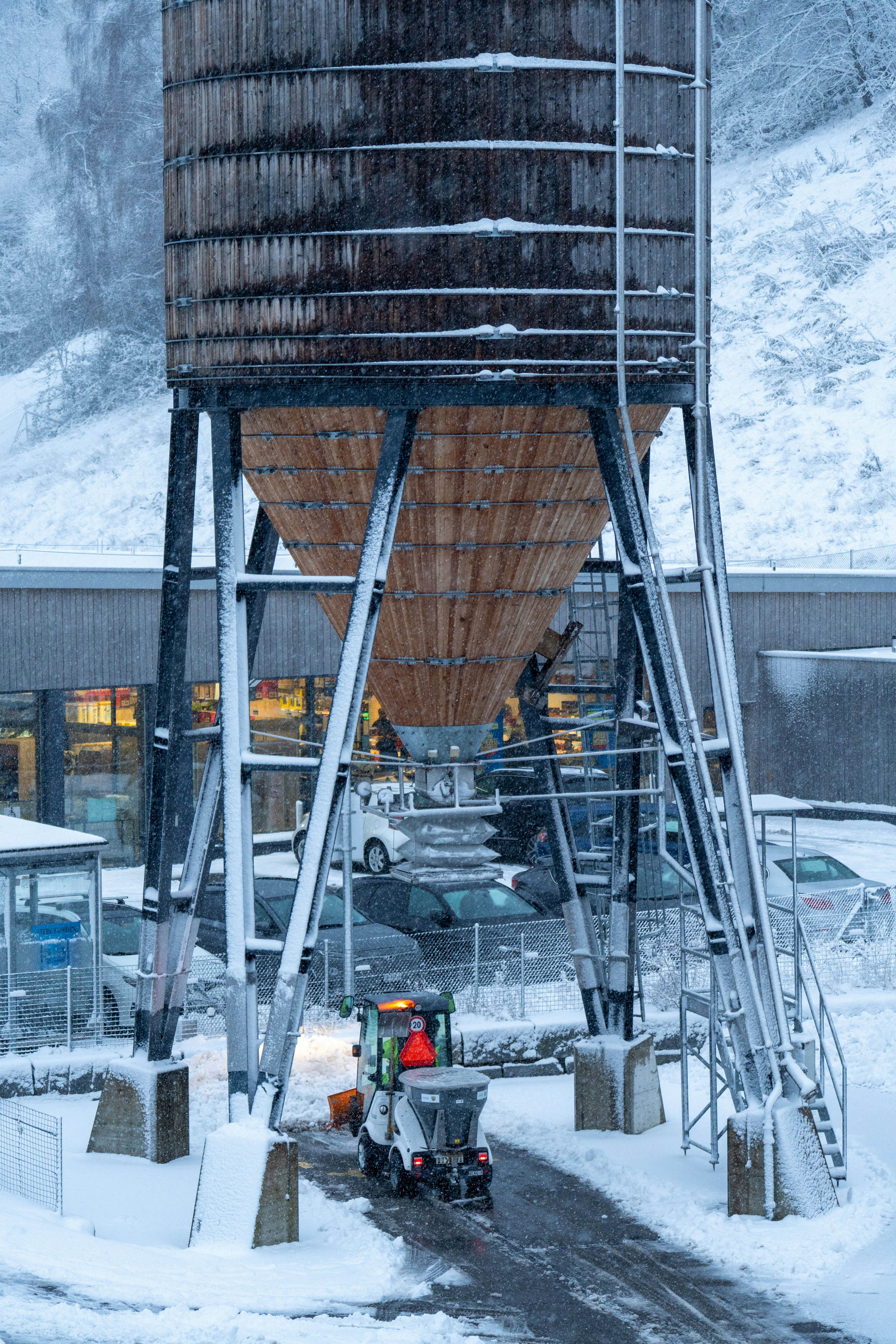Snow plow clearing path near large industrial silo