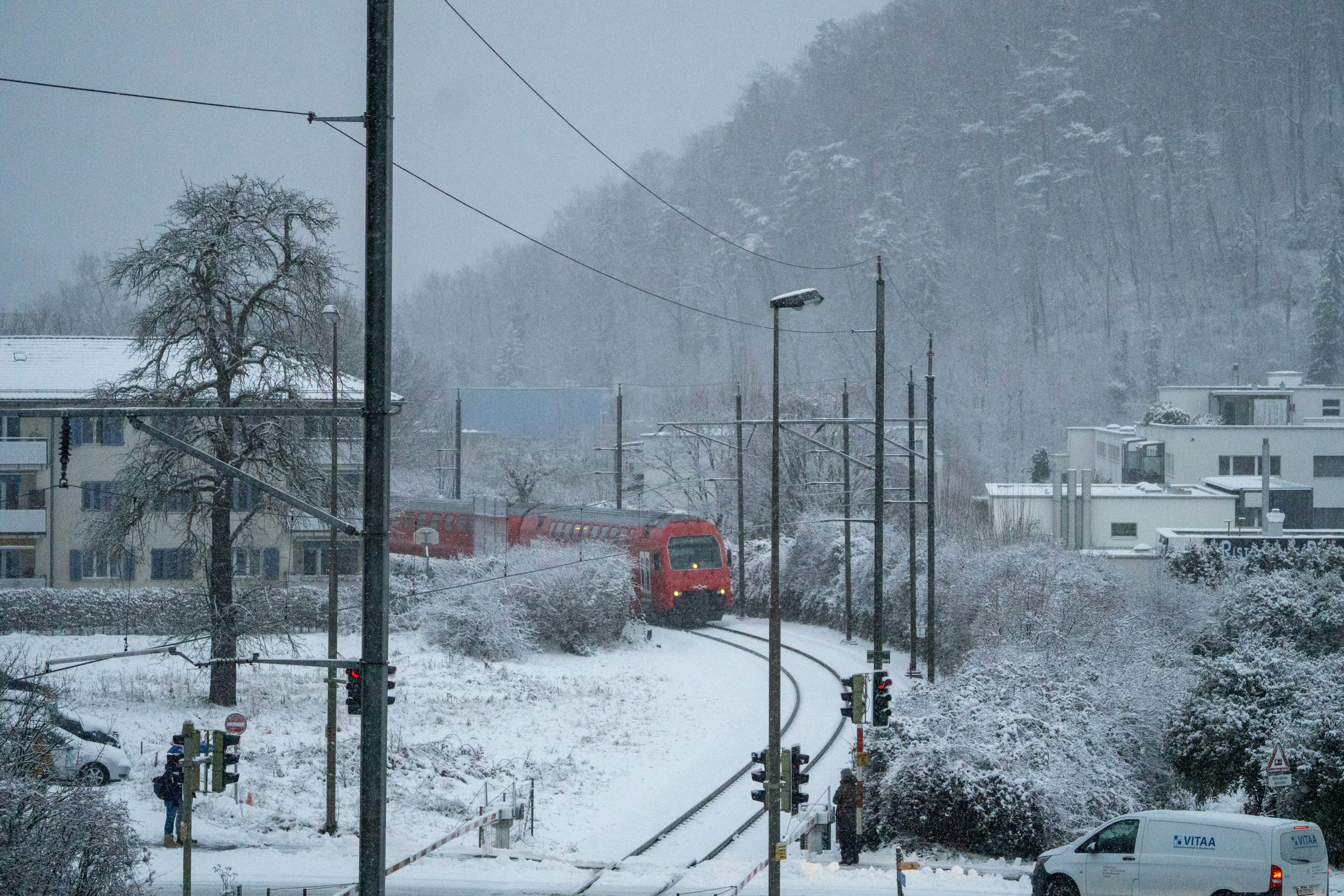 A red train travels on tracks through a snowy landscape.