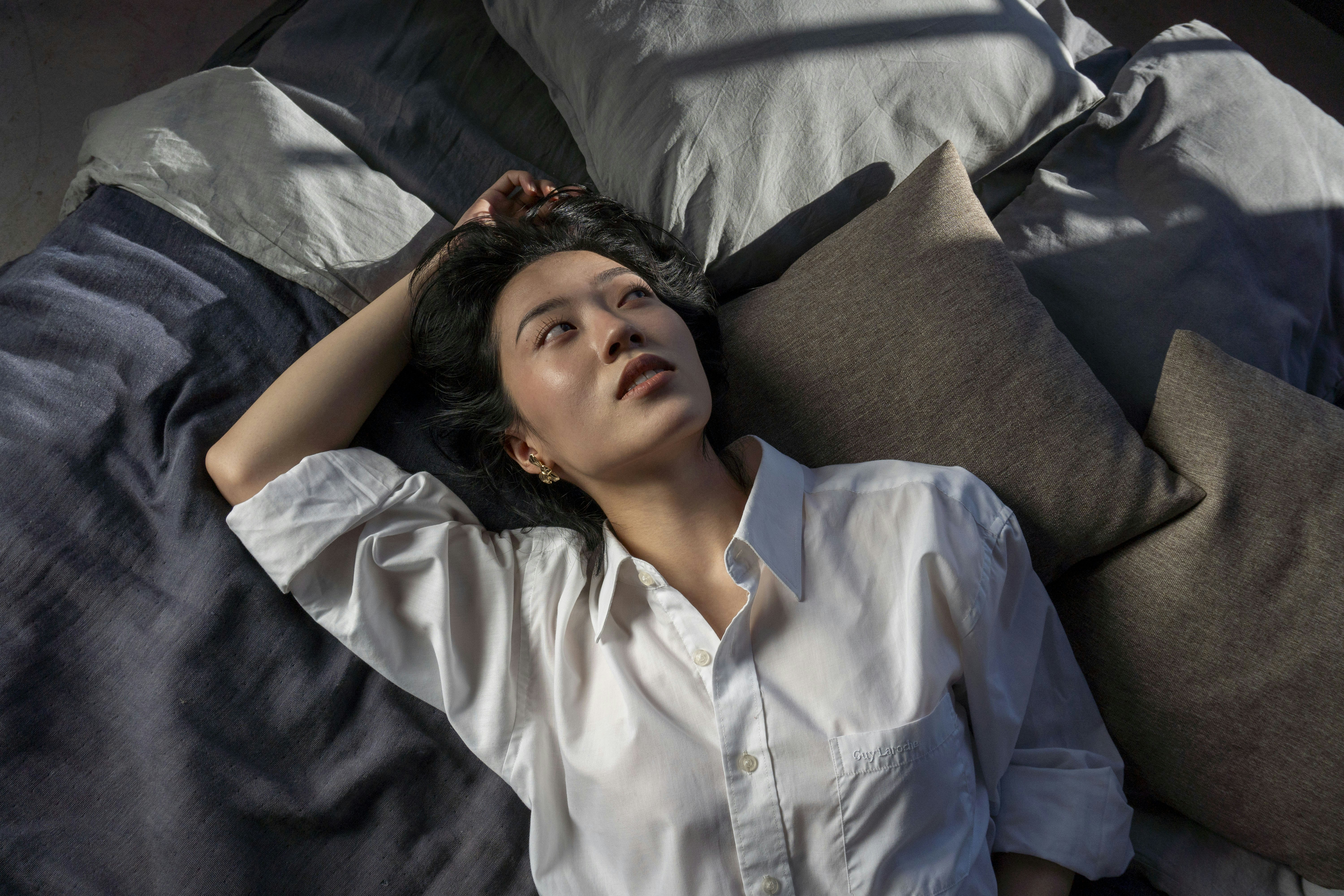 A woman in a white shirt lies on a bed.