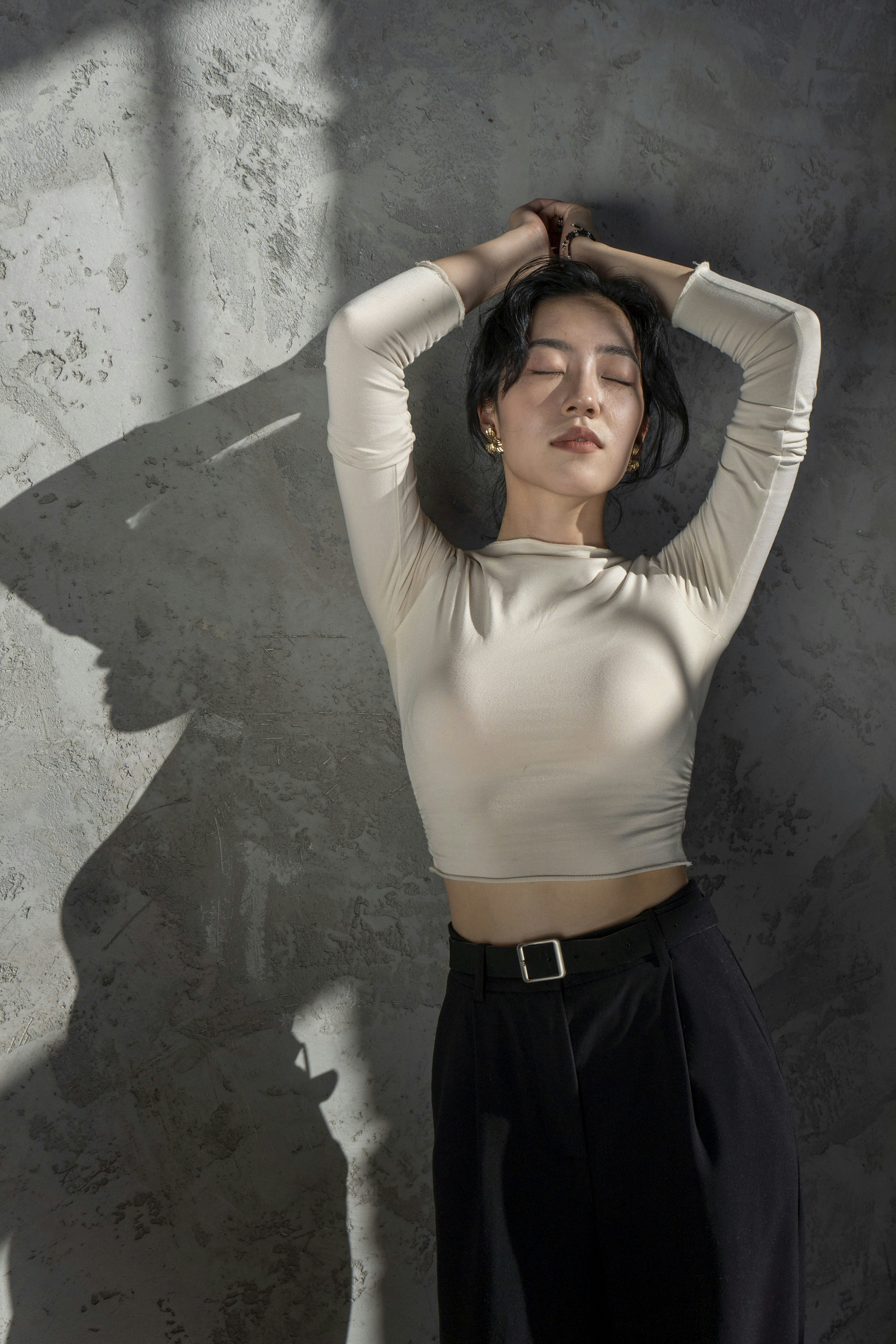 A woman with eyes closed leans against a textured wall.