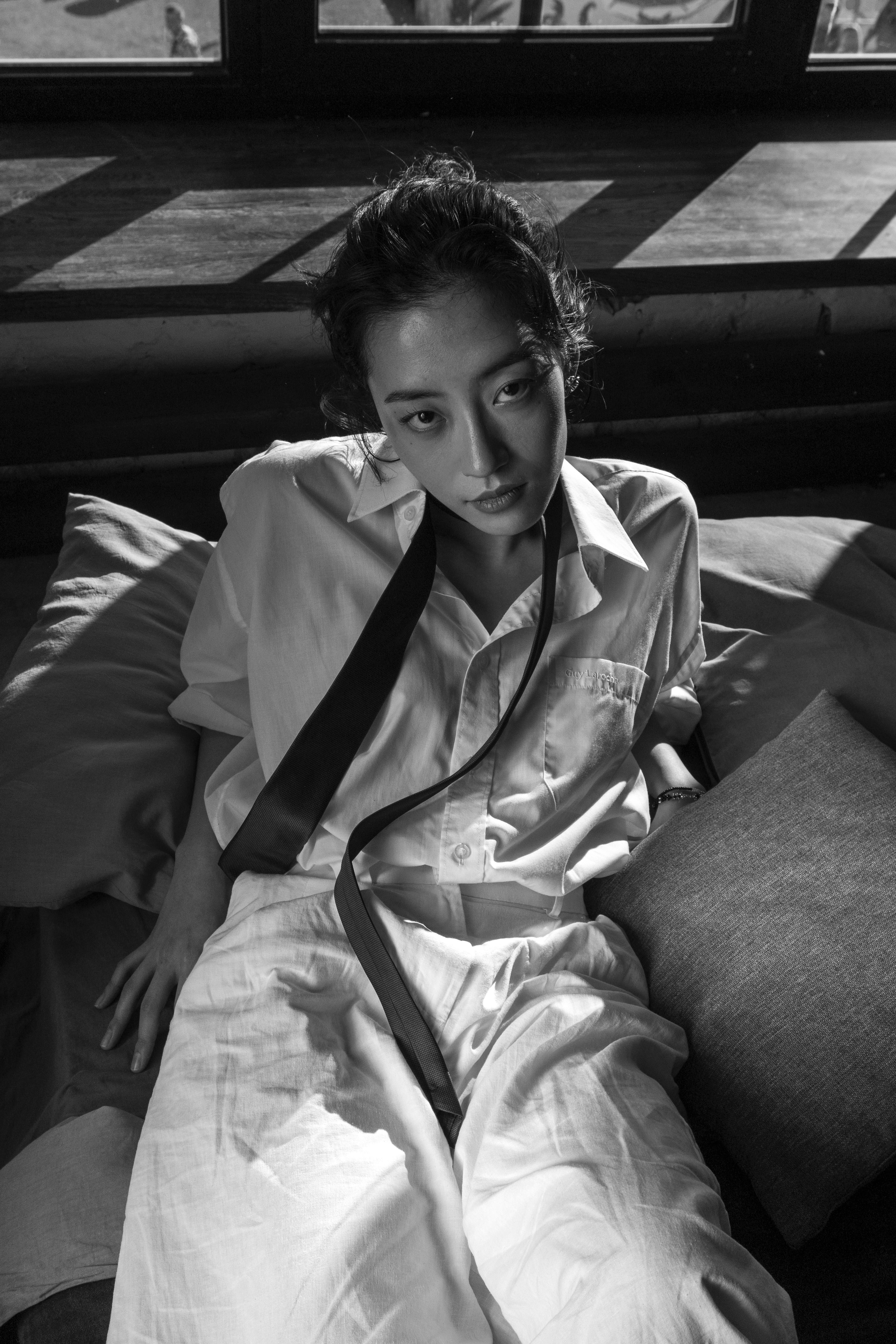 Woman in white shirt and tie sits on pillows.