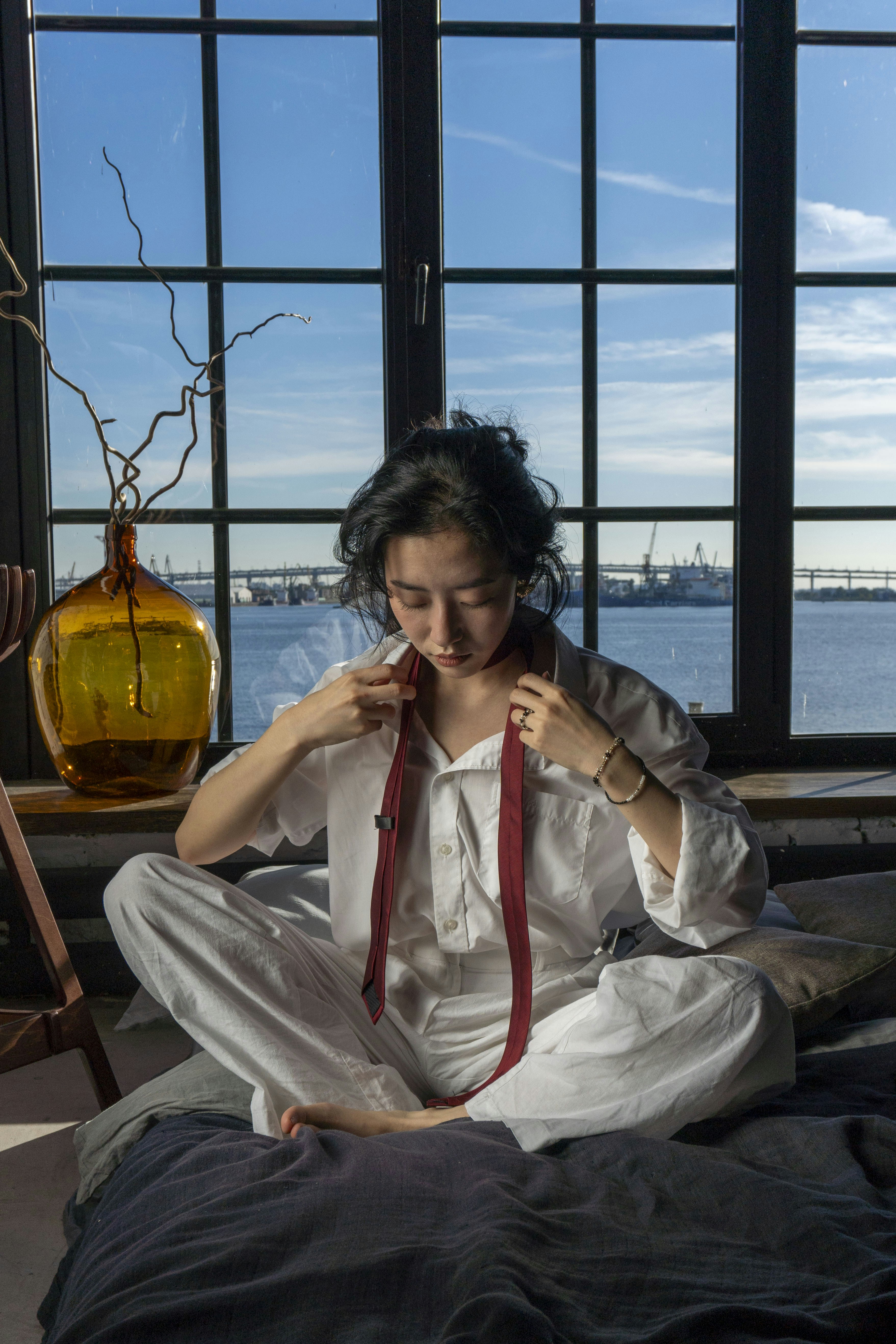 Woman tying a red tie in front of window