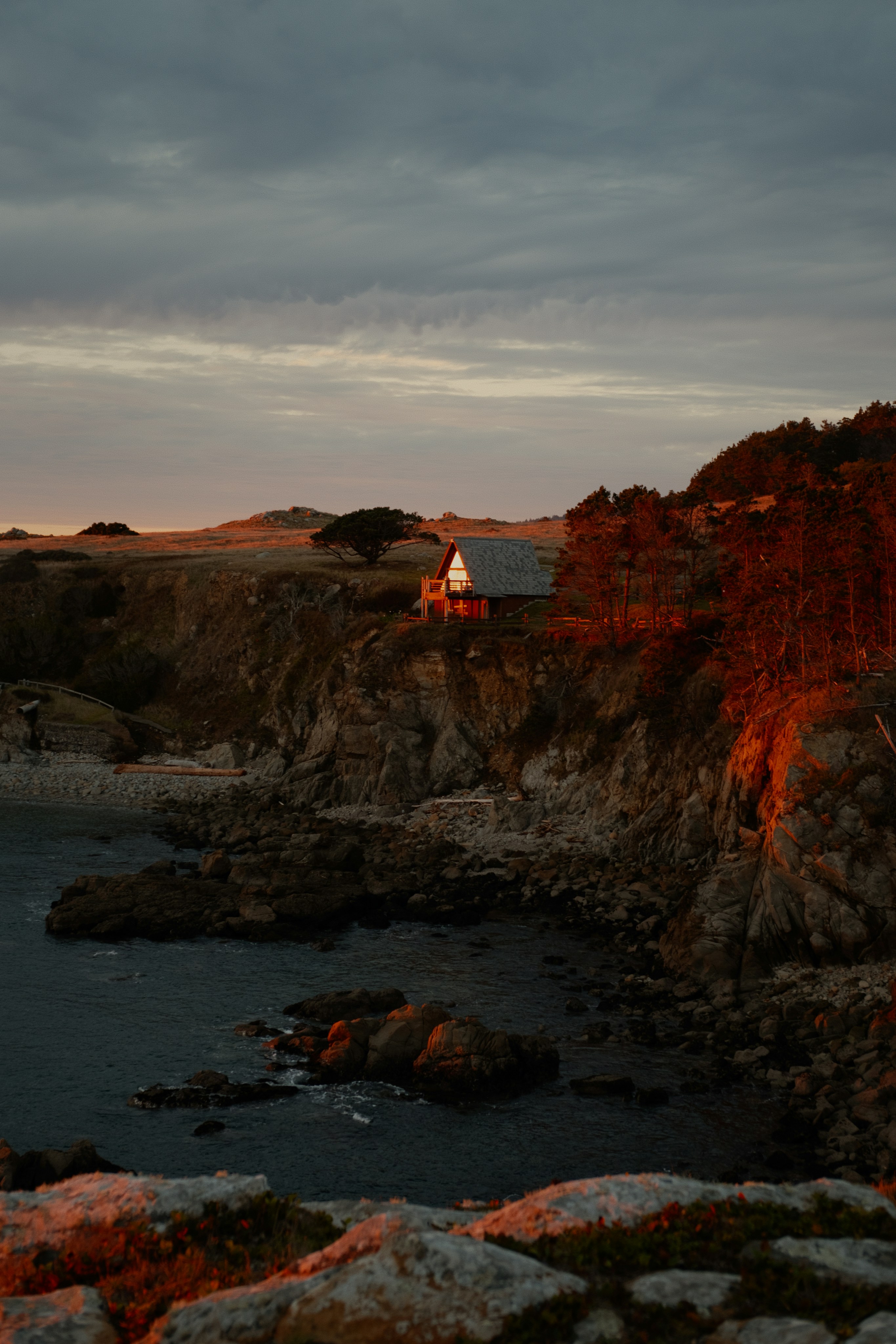 Coastal cabin bathed in warm sunset light on cliffside.