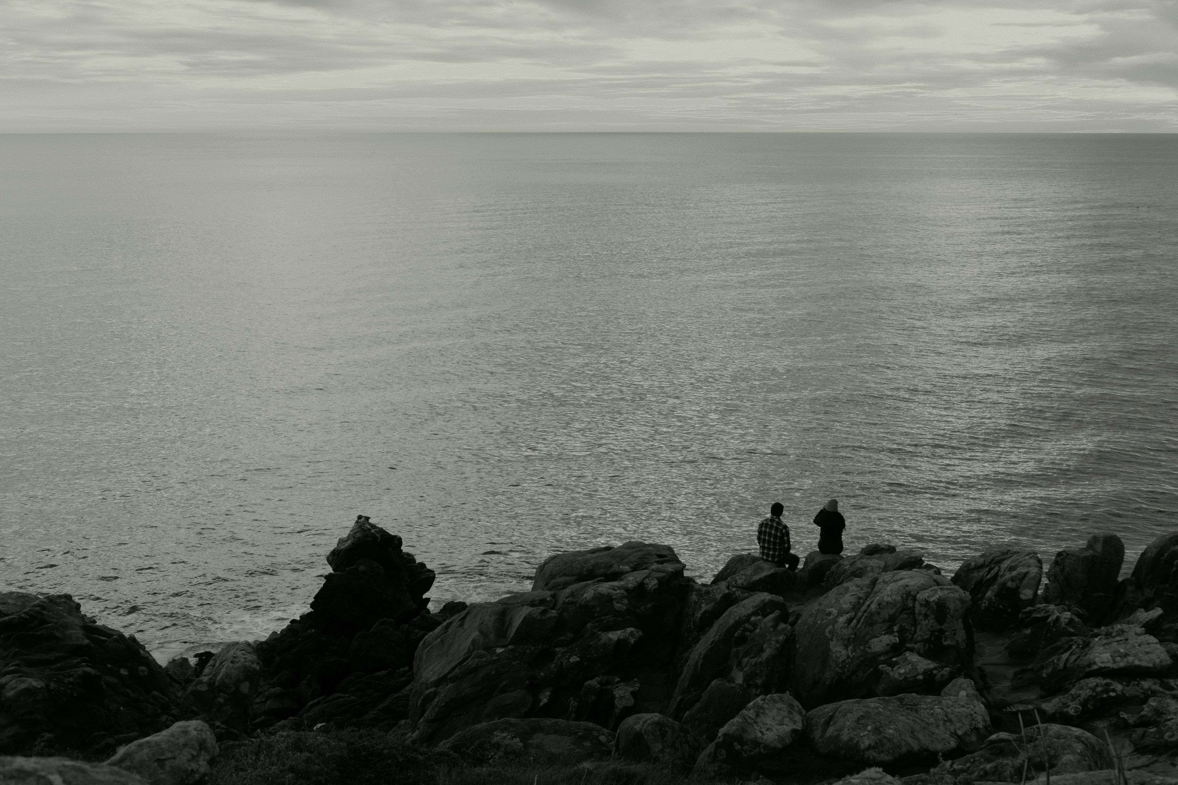 Two people stand on rocky shore overlooking ocean